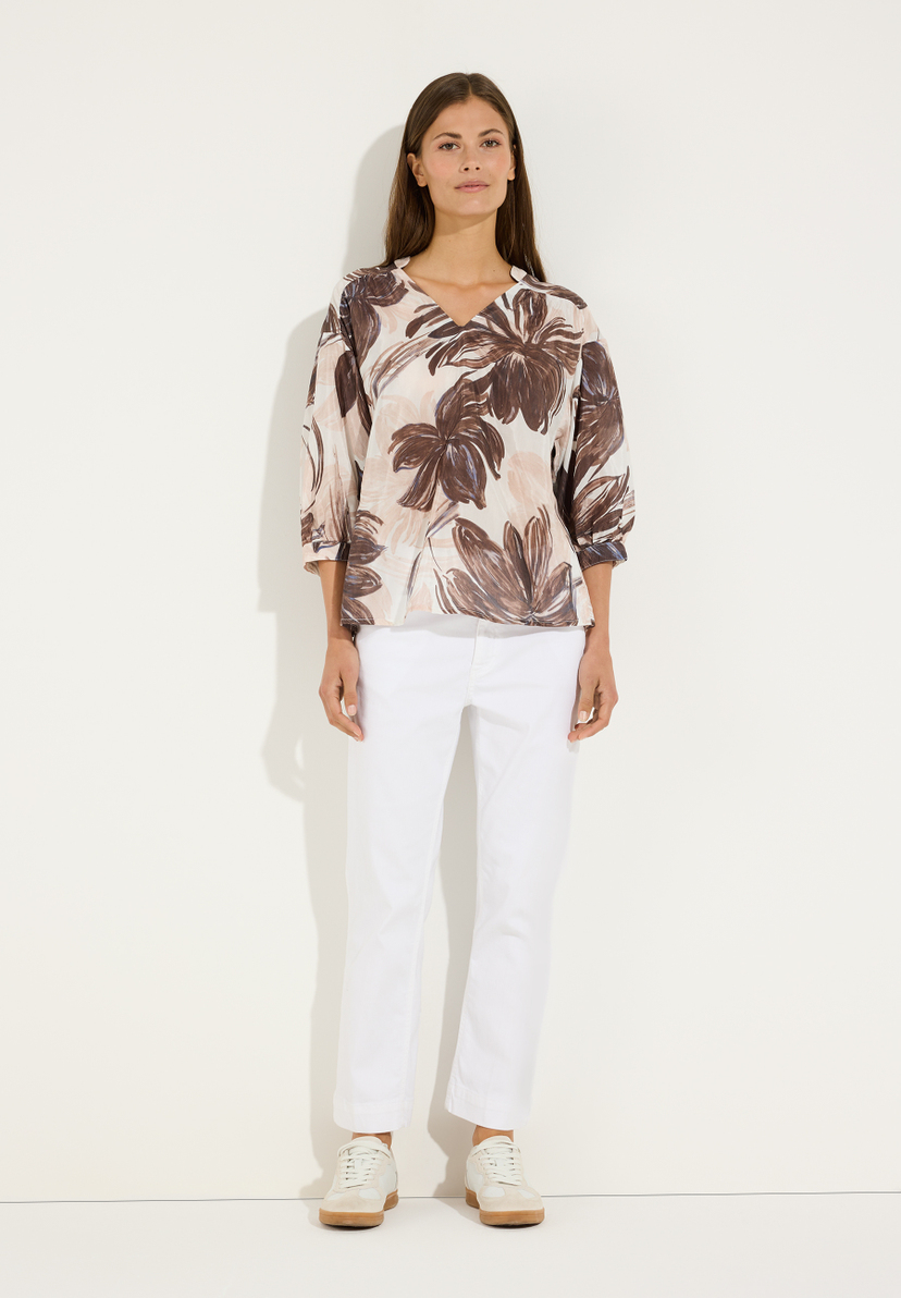 MORE & MORE Damen-Bluse mit V-Ausschnitt, 3/4-Ärmeln und braunem Blumenmuster, kombiniert mit weißer Hose und beigen Sneakern. MORE & MORE Damen-Bluse mit V-Ausschnitt, 3/4-Ärmeln und braunem Blumenmuster, kombiniert mit weißer Hose und beigen Sneakern.