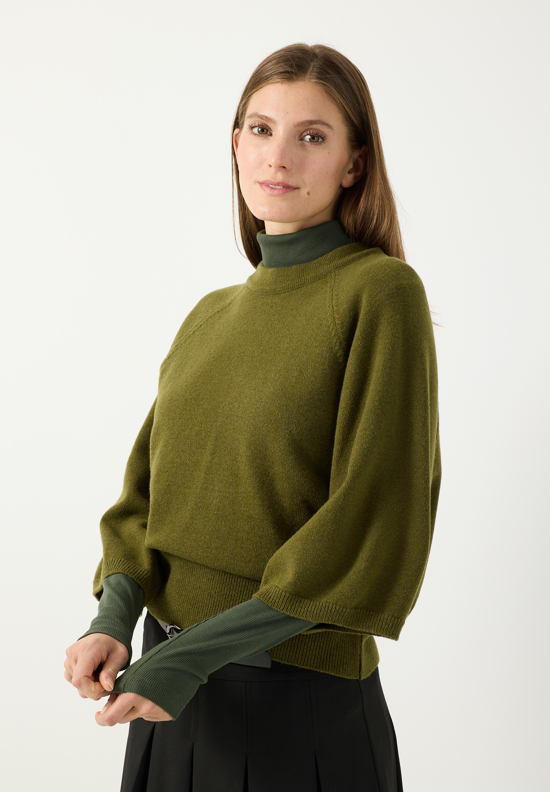 MORE & MORE Pullover: Asiatisches Model in lockerem, gestricktem Pullover in Olivgrün über weißer Bluse mit Schleife und schwarzer Hose.
