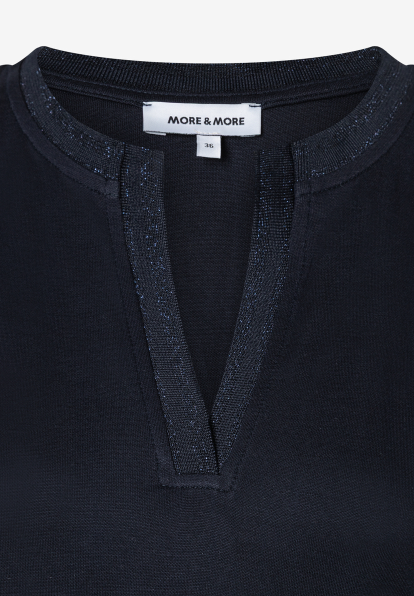 Nahaufnahme eines MORE & MORE Oberteils mit Jersey-Material und V-Ausschnitt. Nahaufnahme eines MORE & MORE Oberteils mit Jersey-Material und V-Ausschnitt.