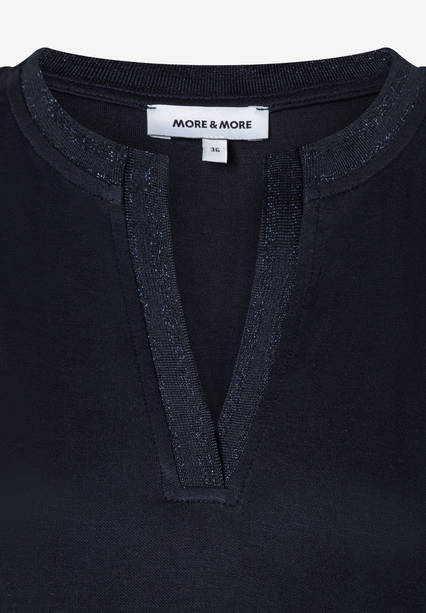 Nahaufnahme eines MORE & MORE Oberteils mit Jersey-Material und V-Ausschnitt. Nahaufnahme eines MORE & MORE Oberteils mit Jersey-Material und V-Ausschnitt.