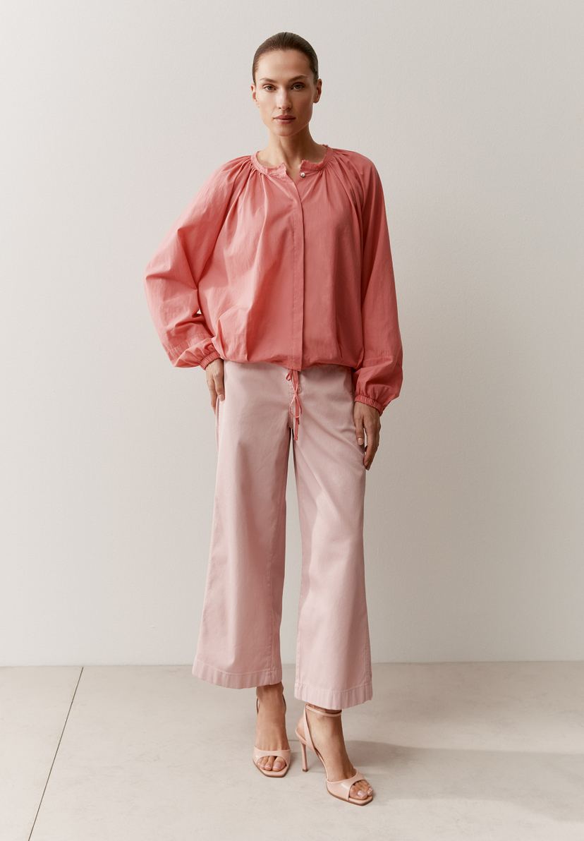 Eine Frau in MORE & MORE Bluse und Hose, beide in Rosatönen, vor einer hellen Wand. Eine Frau in MORE & MORE Bluse und Hose, beide in Rosatönen, vor einer hellen Wand.