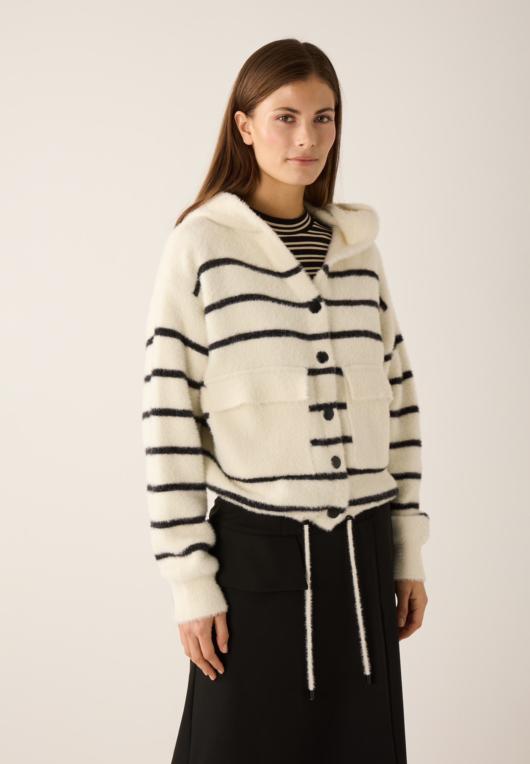 Eine Frau trägt einen gestreiften MORE & MORE Cardigan mit Kapuze und schwarzen Knöpfen.