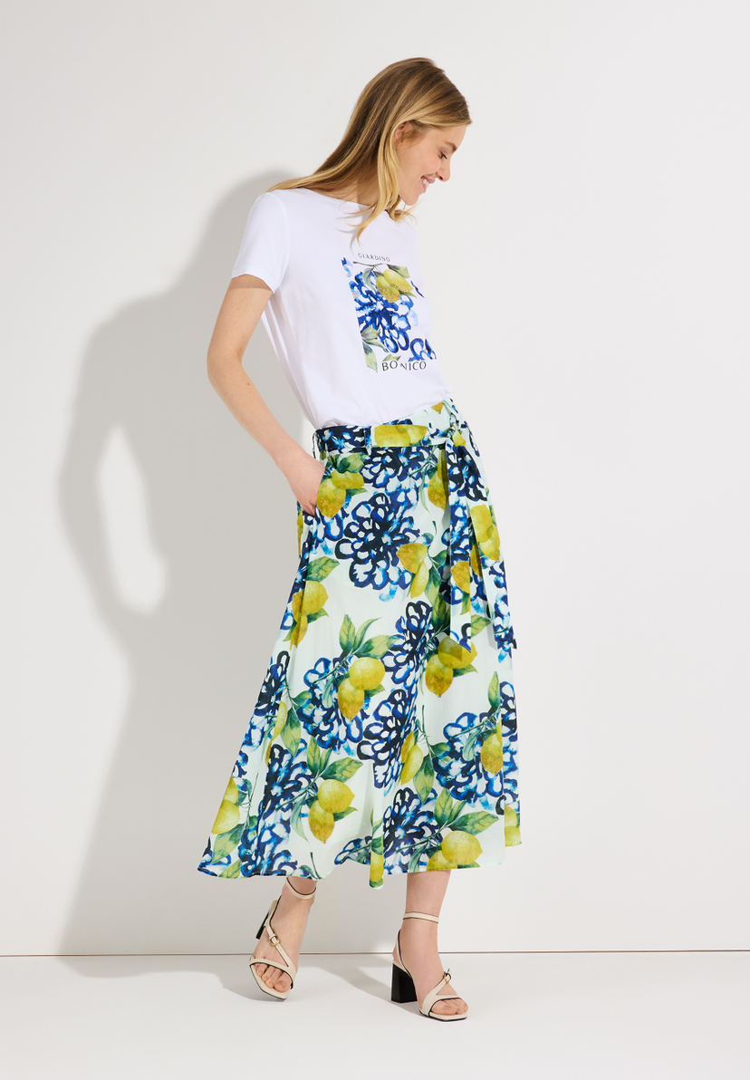 Eine Frau mit MORE & MORE T-Shirt mit Aufdruck und gemustertem Rock. Eine Frau mit MORE & MORE T-Shirt mit Aufdruck und gemustertem Rock.