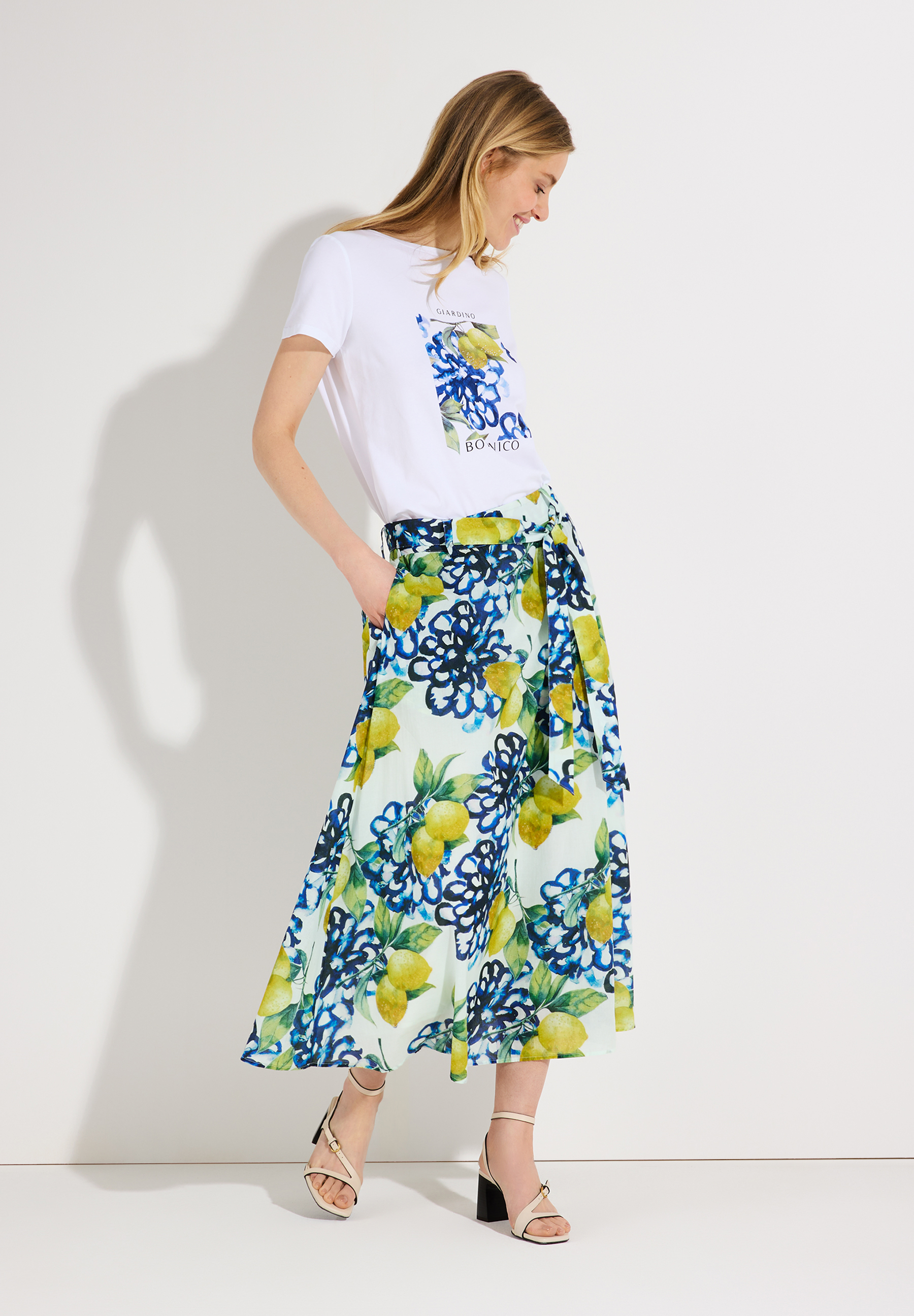 Eine Frau mit MORE & MORE T-Shirt mit Aufdruck und gemustertem Rock. Eine Frau mit MORE & MORE T-Shirt mit Aufdruck und gemustertem Rock.