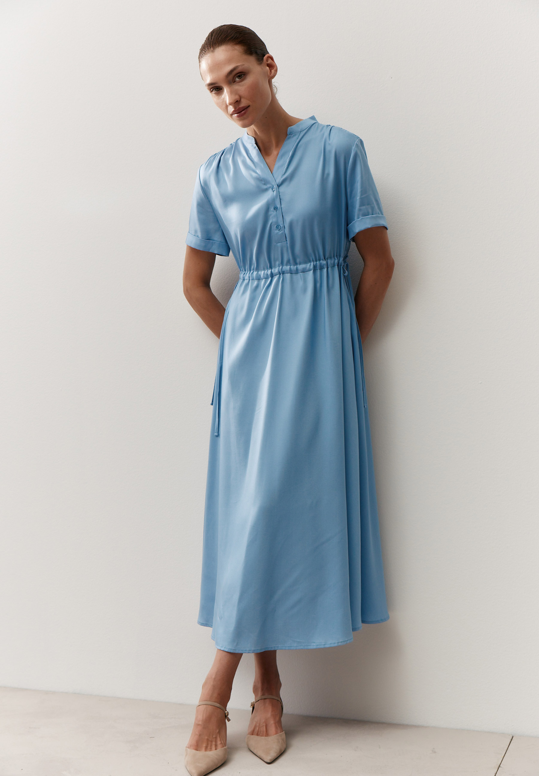 Eine Frau trägt ein hellblaues MORE & MORE Satinkleid. Es ist knielang und leicht tailliert.