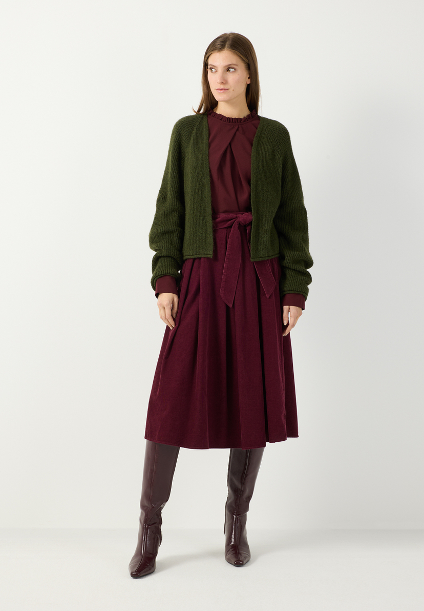 MORE & MORE Cordrock in Beere mit Bindegürtel, kombiniert mit dunkelgrünem Cardigan und hohen Stiefeln. MORE & MORE Cordrock in Beere mit Bindegürtel, kombiniert mit dunkelgrünem Cardigan und hohen Stiefeln.