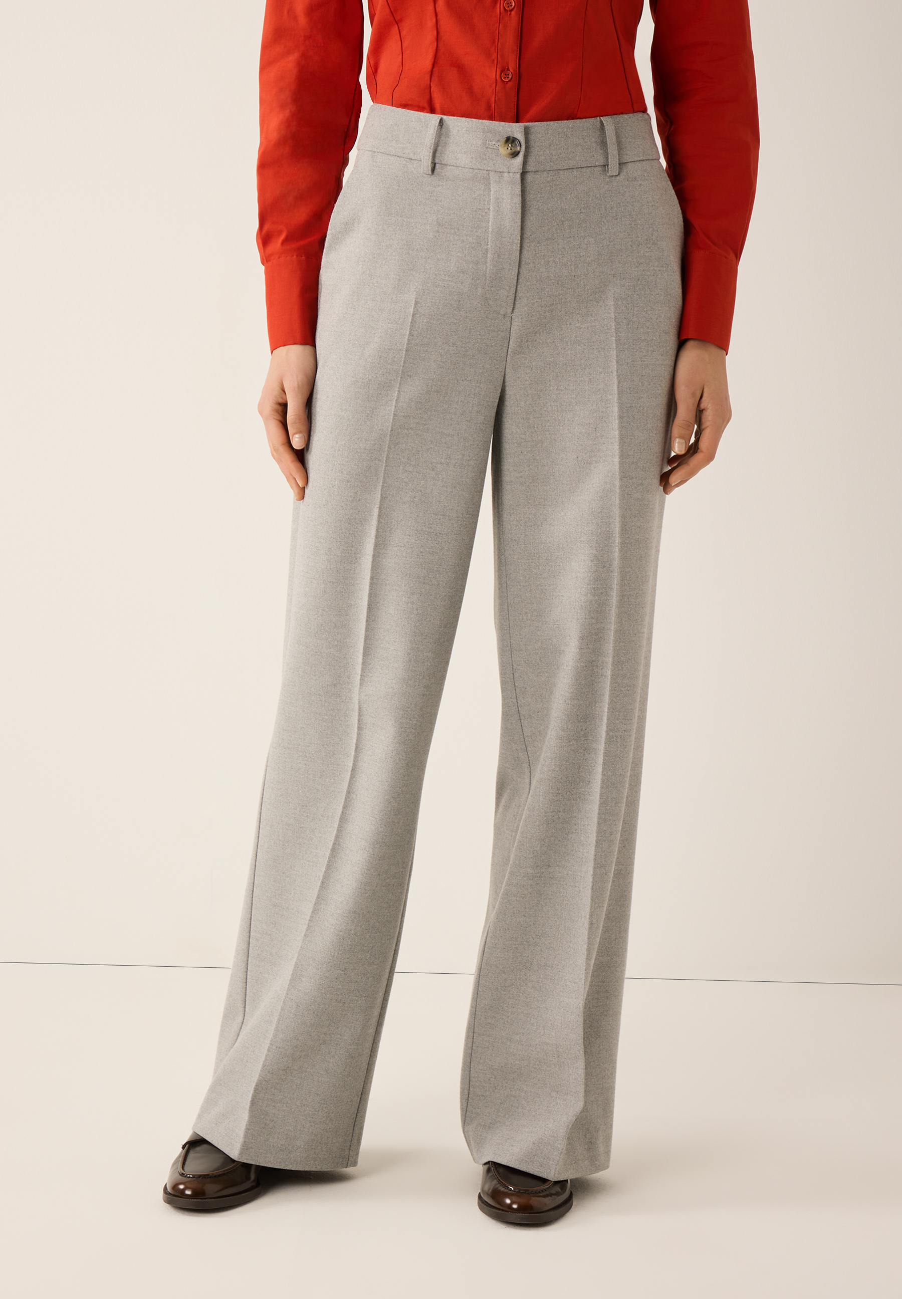 Eine Person trägt eine graue Webware-Hose von MORE & MORE, kombiniert mit einer roten Bluse und braunen Schuhen.