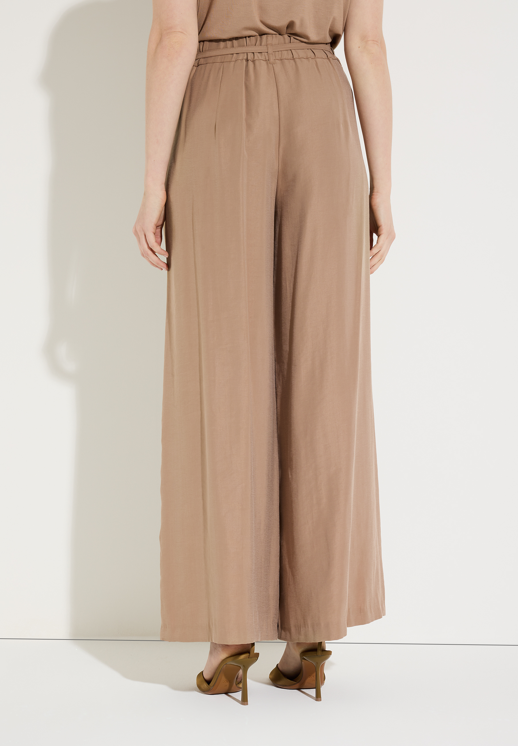 Die MORE & MORE Hose ist weit geschnitten und aus fließendem, beigem Stoff. Hinten wird sie mit einem Band zusammengehalten.