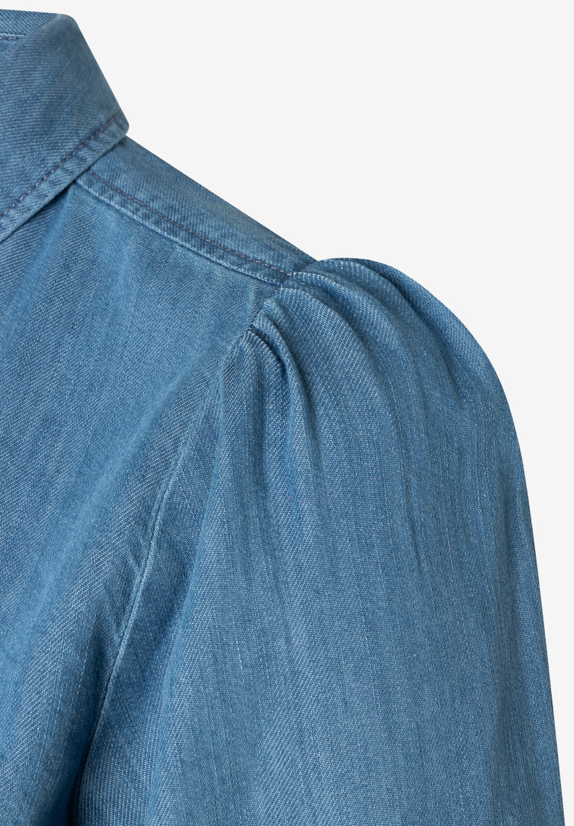 Detailaufnahme einer Denim-Bluse von MORE & MORE mit Puffärmel und Kragen. Detailaufnahme einer Denim-Bluse von MORE & MORE mit Puffärmel und Kragen.
