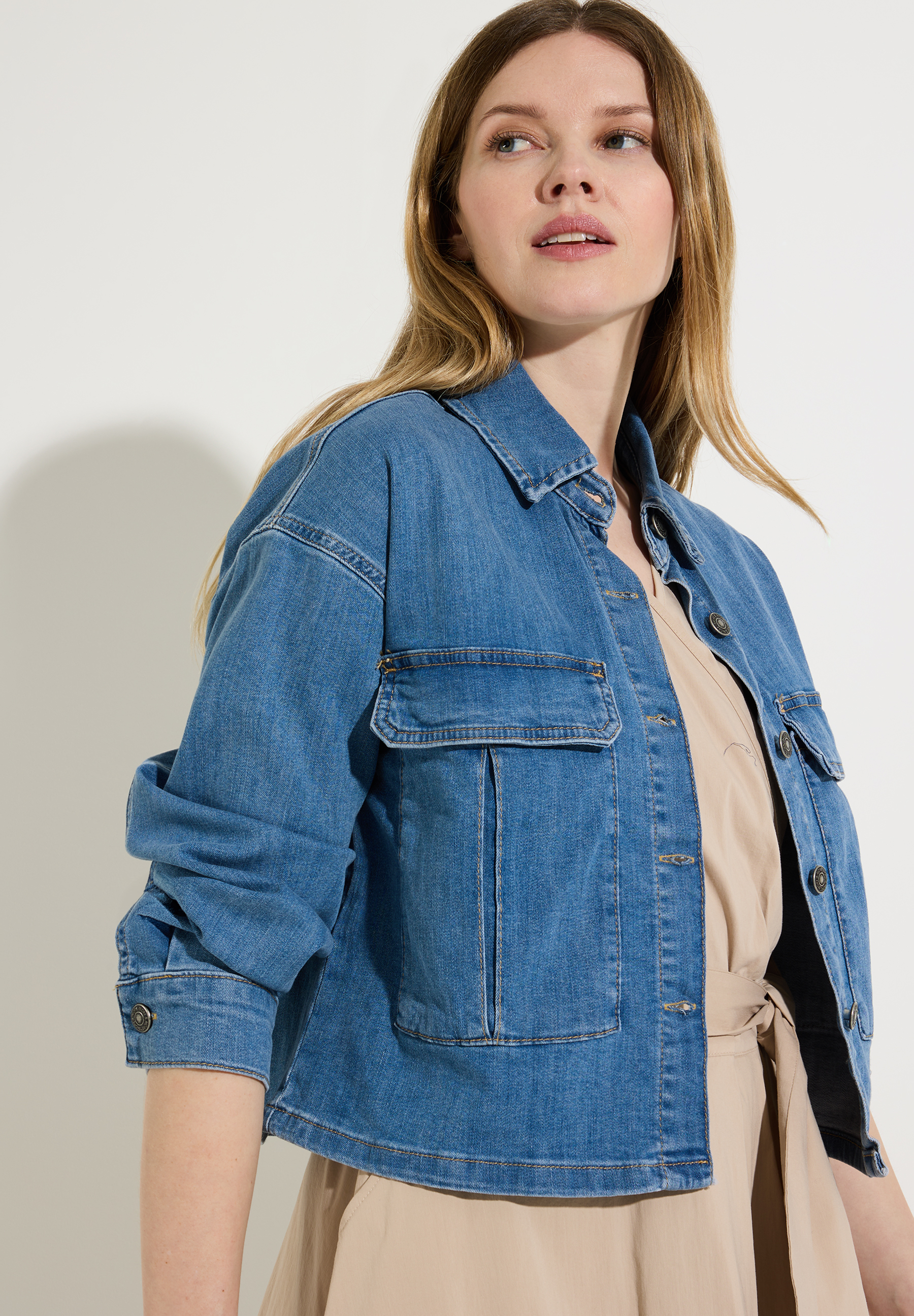 Eine Frau in einer Jeansjacke von MORE & MORE, seitlich vor einem weißen Hintergrund. Eine Frau in einer Jeansjacke von MORE & MORE, seitlich vor einem weißen Hintergrund.