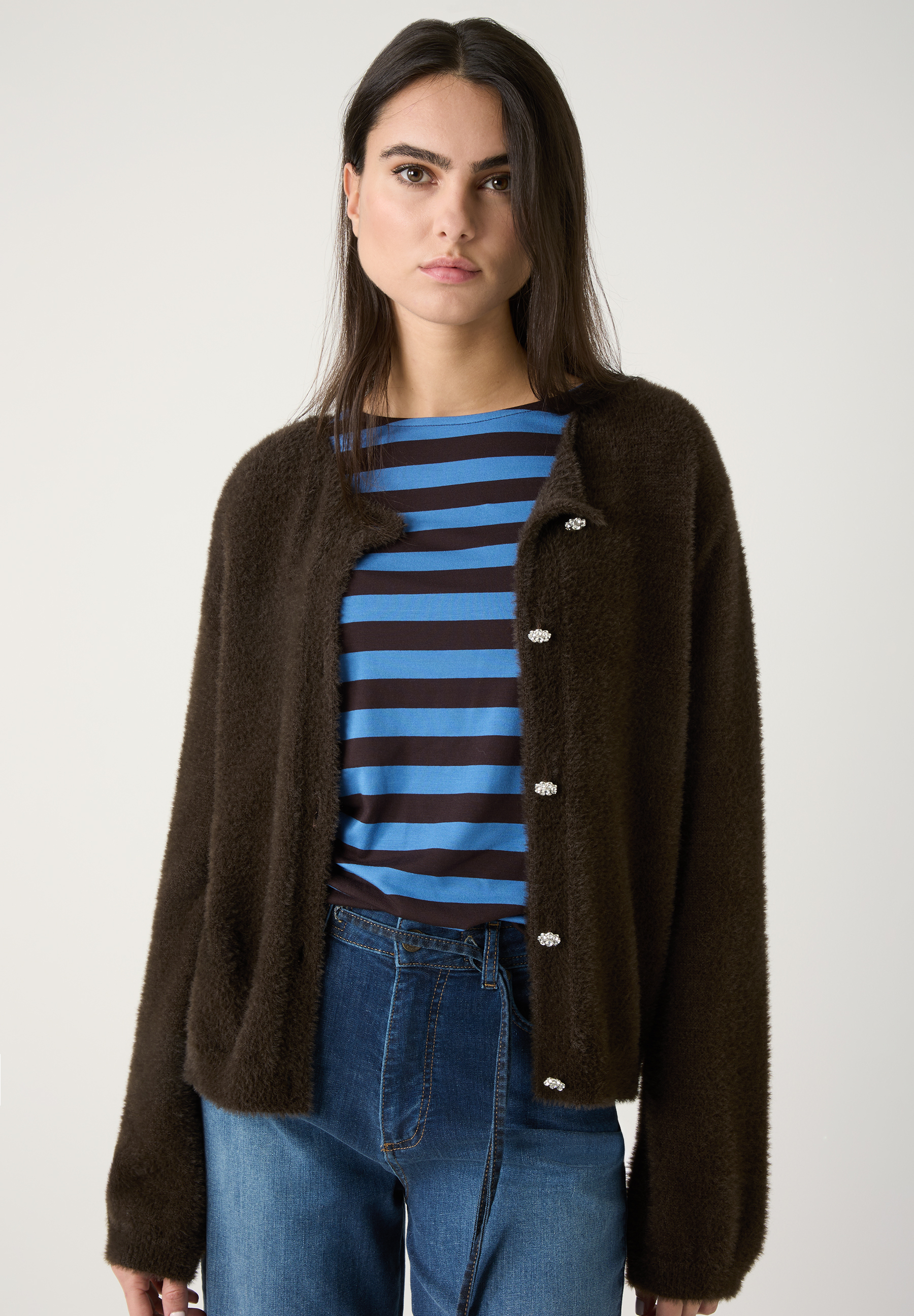Eine Frau mit einem MORE & MORE Oberteil, einem braunen Cardigan, einem blau gestreiften Shirt und einer Jeans.