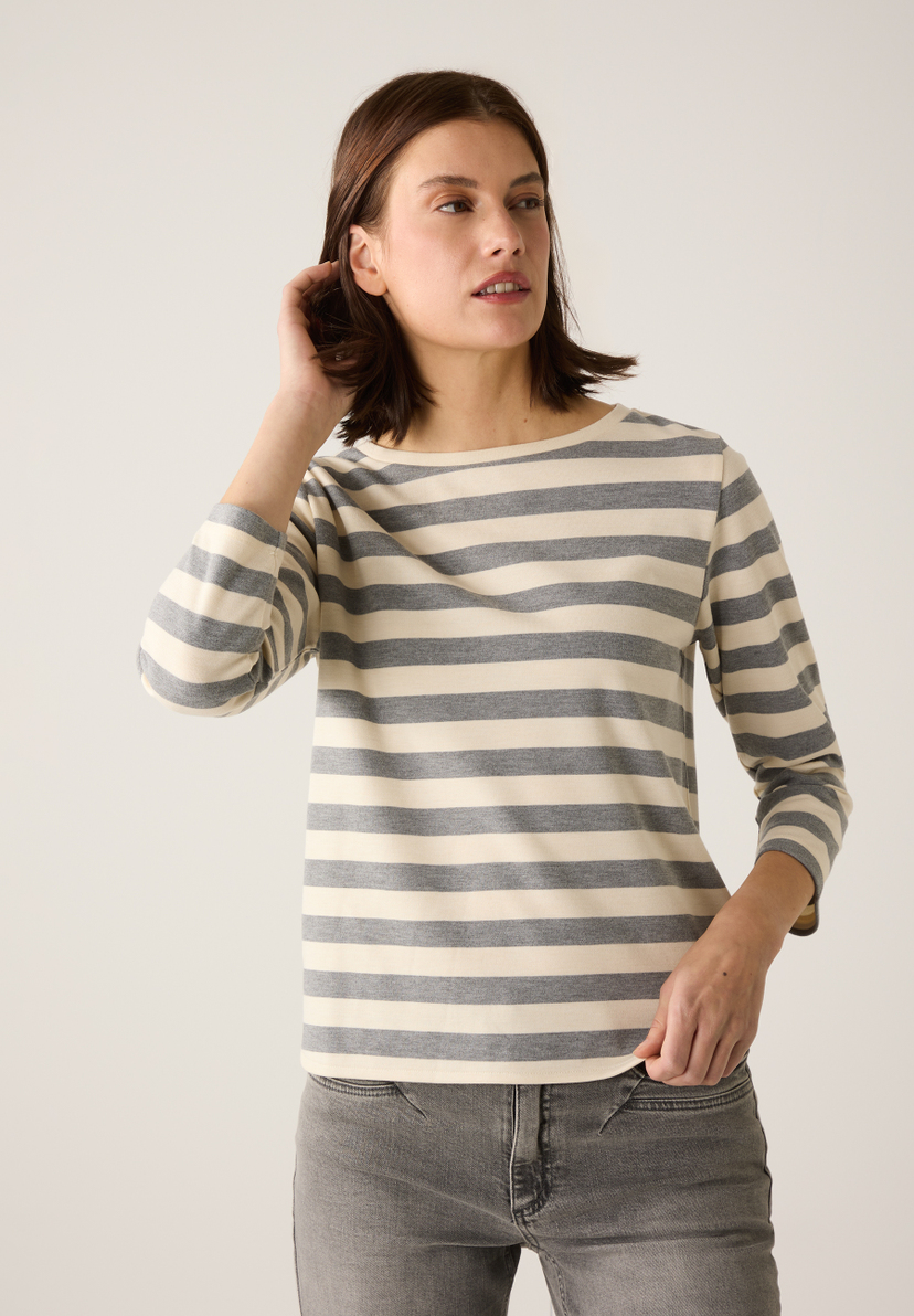 Eine Frau im MORE & MORE-Oberteil mit grauen und weißen Streifen und Jeans. Eine Frau im MORE & MORE-Oberteil mit grauen und weißen Streifen und Jeans.