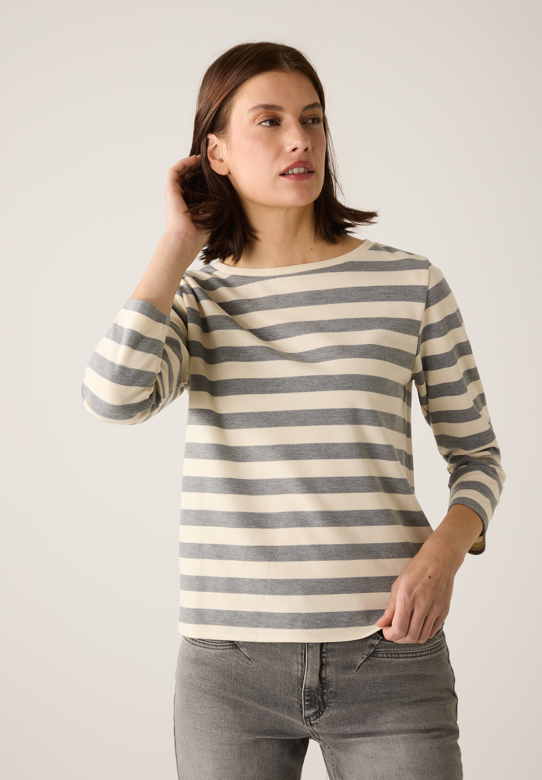 Eine Frau im MORE & MORE-Oberteil mit grauen und weißen Streifen und Jeans. Eine Frau im MORE & MORE-Oberteil mit grauen und weißen Streifen und Jeans.