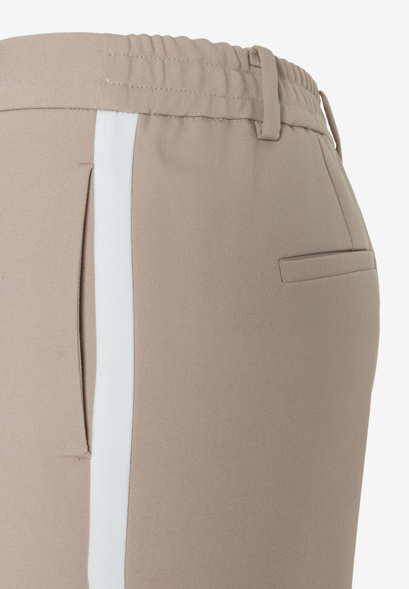 Detailaufnahme einer beigen MORE & MORE Hose mit weißem Seitenstreifen, Webware und Gummibund. Detailaufnahme einer beigen MORE & MORE Hose mit weißem Seitenstreifen, Webware und Gummibund.