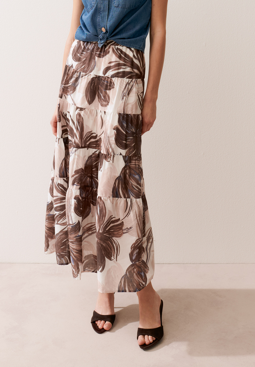 Eine Frau trägt einen MORE & MORE Rock mit Blumenmuster, ein Jeanshemd und schwarze Sandalen. Eine Frau trägt einen MORE & MORE Rock mit Blumenmuster, ein Jeanshemd und schwarze Sandalen.