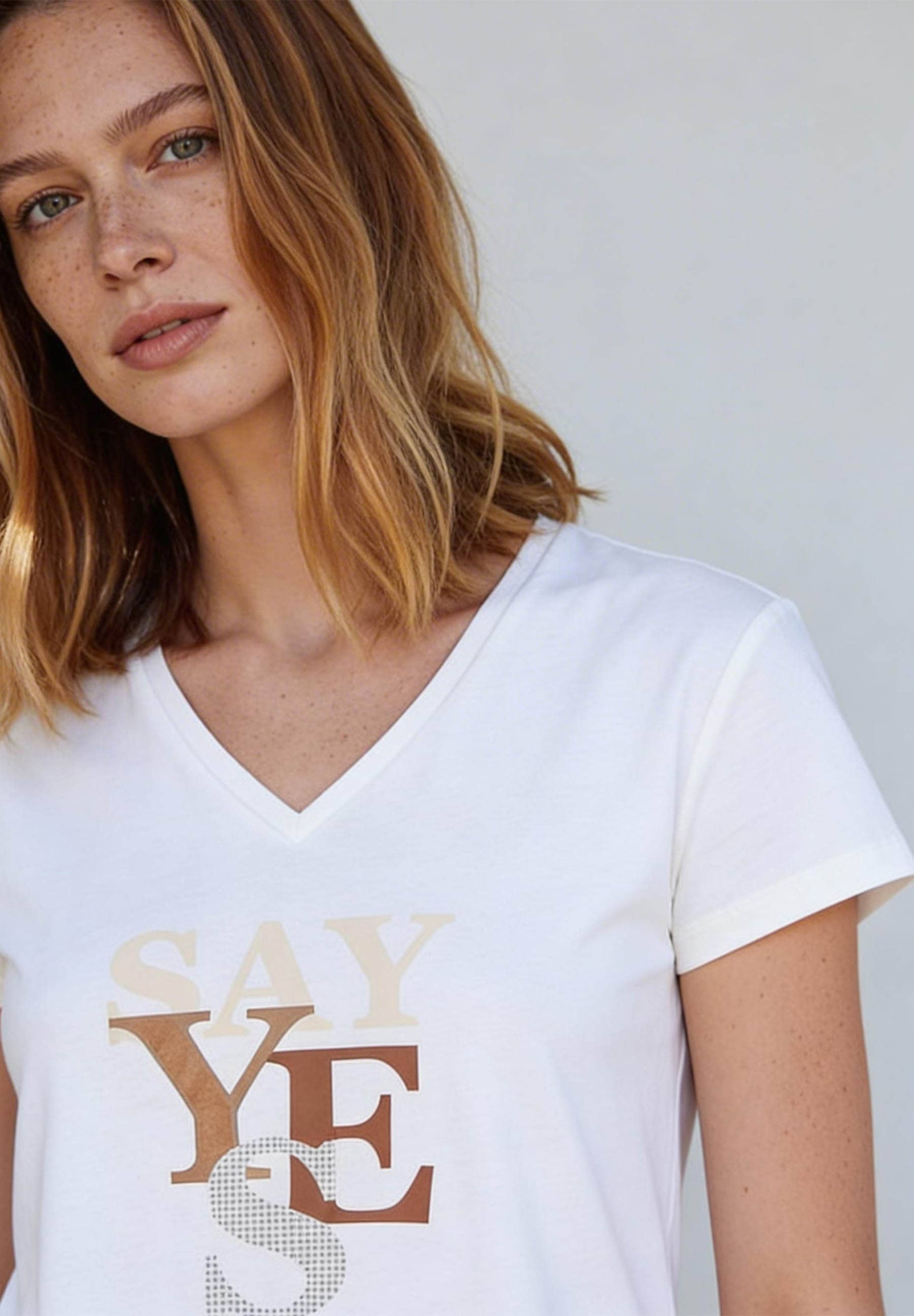 Porträt einer Frau mit Sommersprossen, die ein weißes T-Shirt von MORE & MORE mit dem Aufdruck 'Say Yes' trägt.