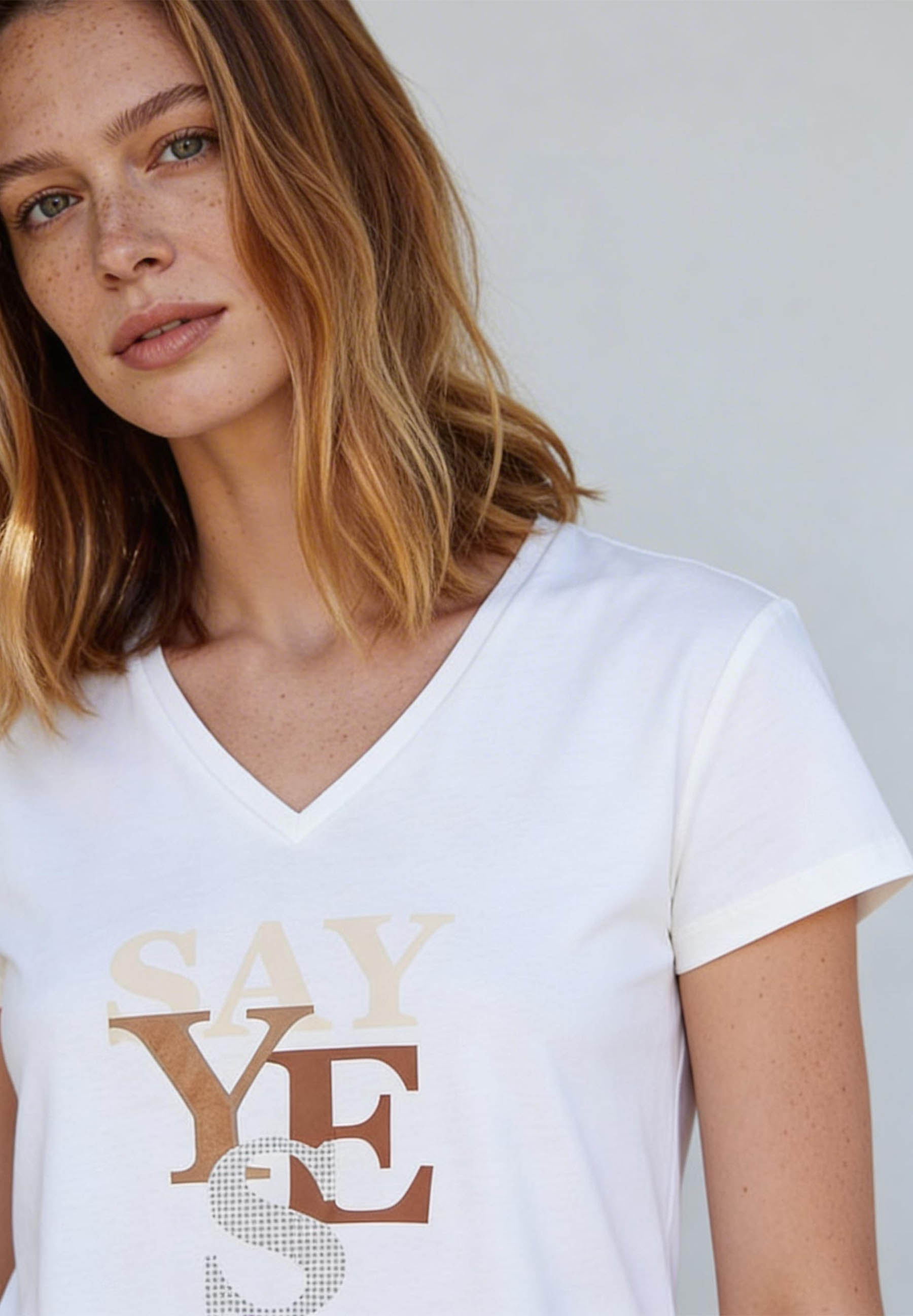 AI generated - Porträt einer Frau mit Sommersprossen, die ein weißes T-Shirt von MORE & MORE mit dem Aufdruck 'Say Yes' trägt. AI generated - Porträt einer Frau mit Sommersprossen, die ein weißes T-Shirt von MORE & MORE mit dem Aufdruck 'Say Yes' trägt.