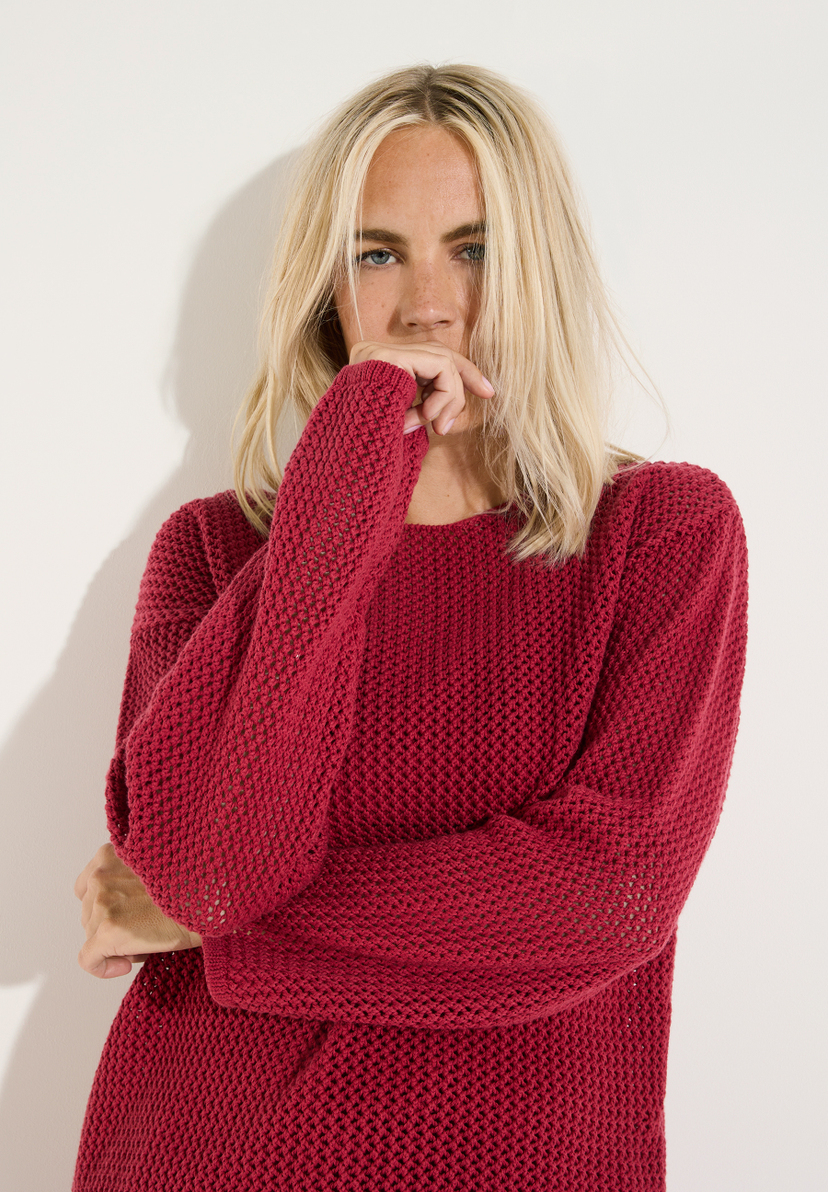 MORE & MORE Pullover in Rot, getragen von einer blonden Frau, die ihre Hand bedeckt und in die Kamera blickt. MORE & MORE Pullover in Rot, getragen von einer blonden Frau, die ihre Hand bedeckt und in die Kamera blickt.