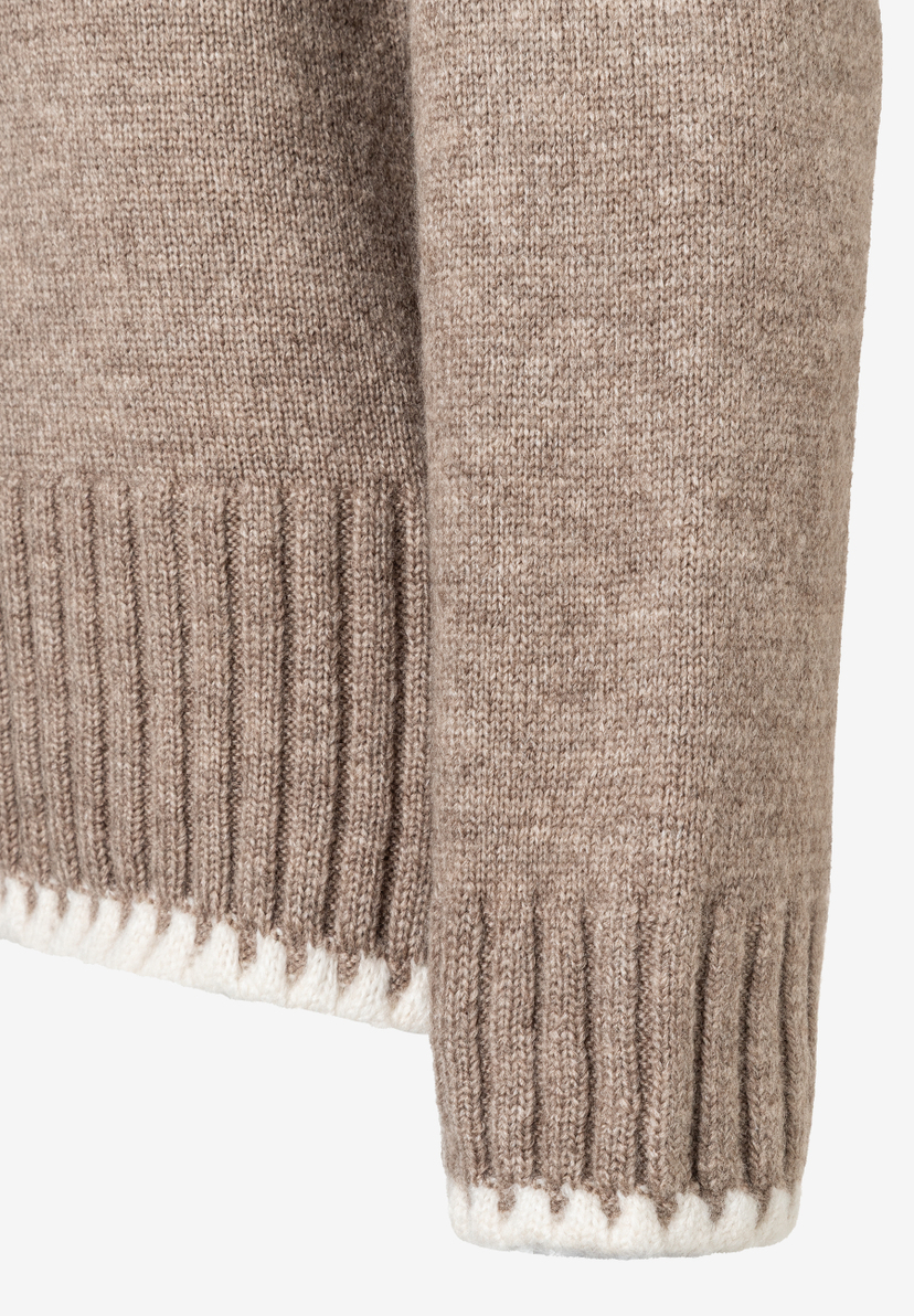 Nahaufnahme eines MORE & MORE Strickpullovers. Die Ärmel sind hellbraun gestrickt und haben ein weißes Zickzackmuster am Abschluss. Nahaufnahme eines MORE & MORE Strickpullovers. Die Ärmel sind hellbraun gestrickt und haben ein weißes Zickzackmuster am Abschluss.