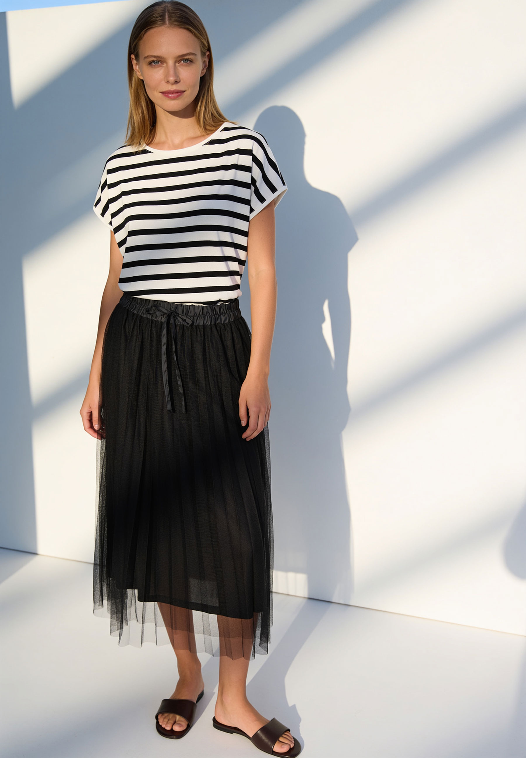 MORE & MORE schwarzer elastischer Mesh-Rock mit Bindeband kombiniert mit einem gestreiften Shirt, getragen von einer Frau MORE & MORE schwarzer elastischer Mesh-Rock mit Bindeband kombiniert mit einem gestreiften Shirt, getragen von einer Frau