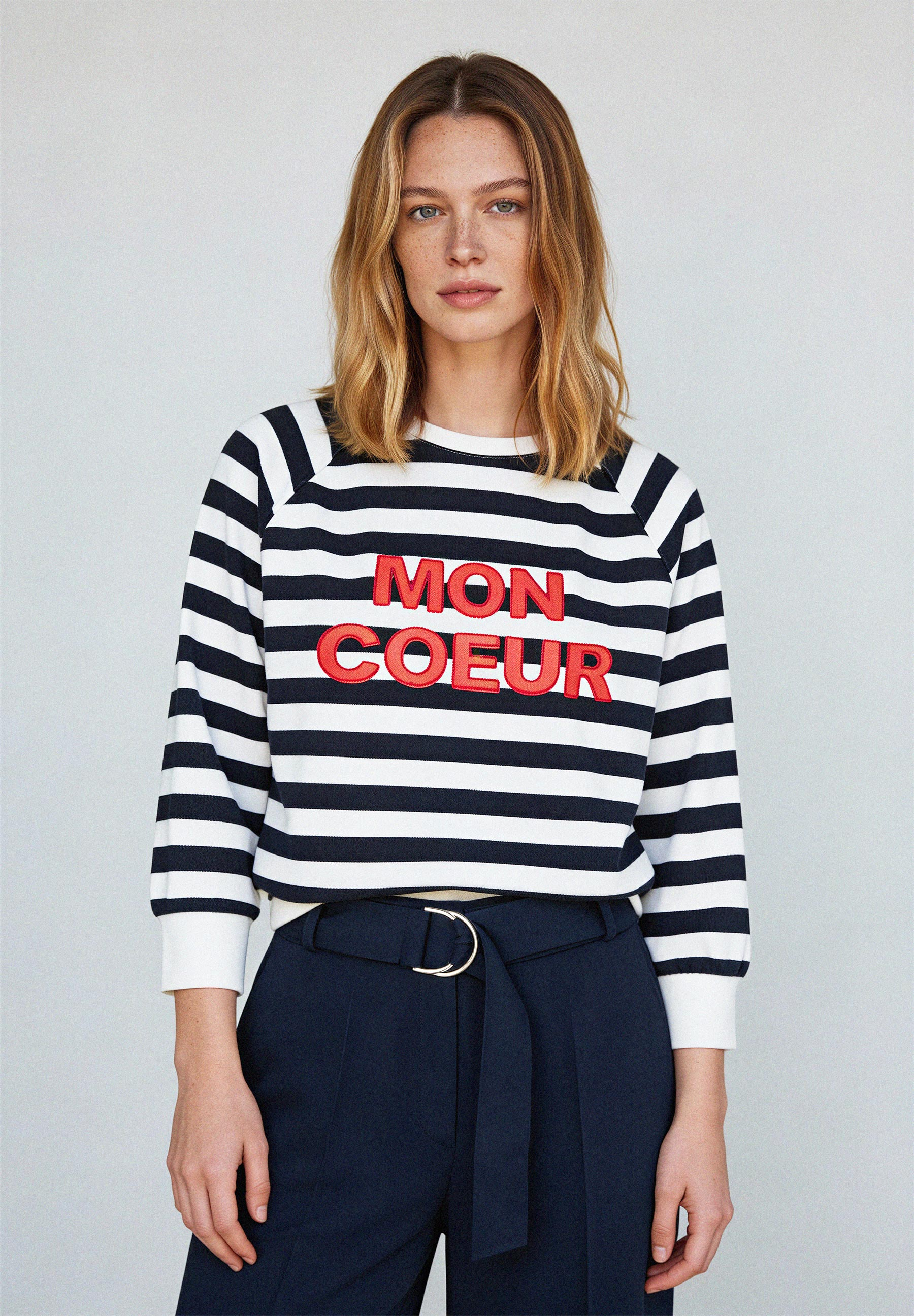 AI generated - Eine Frau trägt ein MORE & MORE-Sweatshirt mit "Mon Coeur"-Aufschrift und eine dunkle Hose. AI generated - Eine Frau trägt ein MORE & MORE-Sweatshirt mit "Mon Coeur"-Aufschrift und eine dunkle Hose.