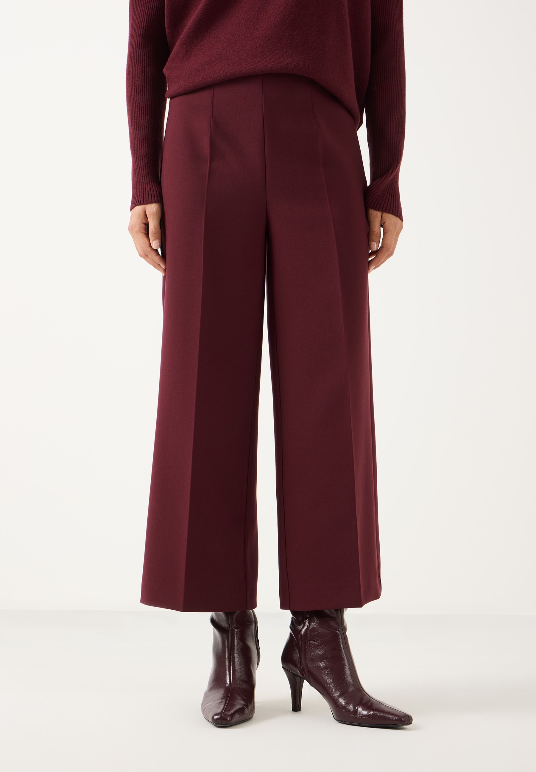 MORE & MORE Hose in Dunkelrot, weit geschnitten mit schmaler Taille und passendem Pullover sowie Stiefeletten.