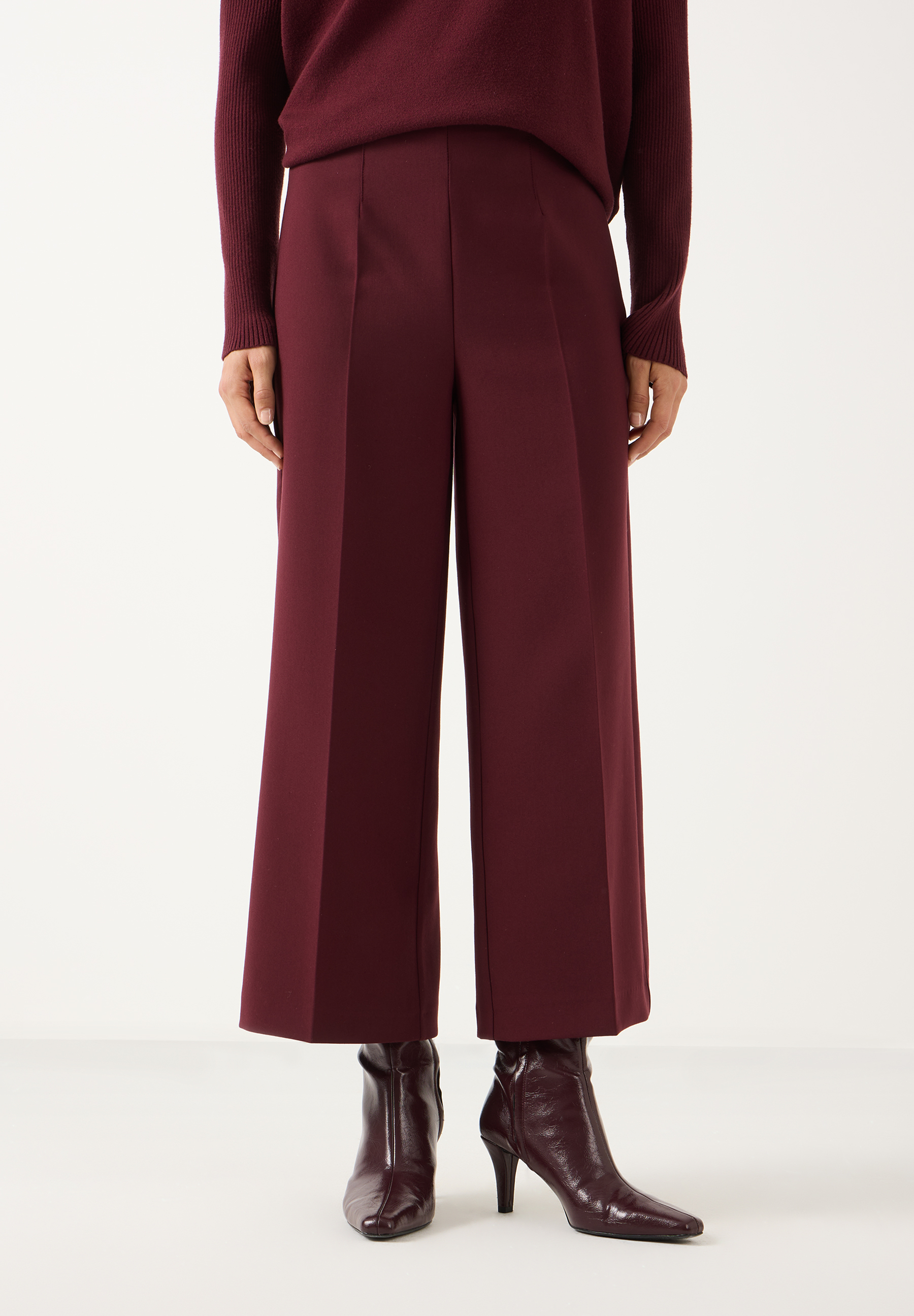 MORE & MORE Hose in Dunkelrot, weit geschnitten mit schmaler Taille und passendem Pullover sowie Stiefeletten.