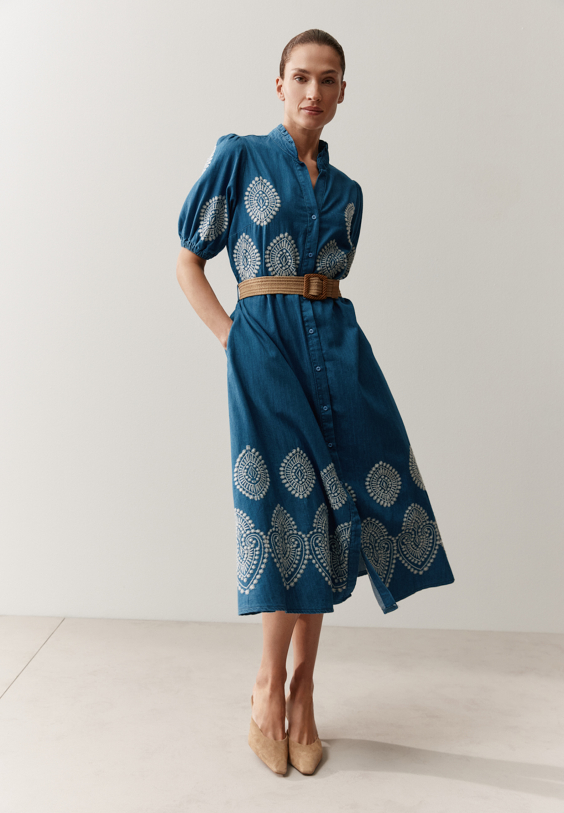 Eine Frau, die ein blaues MORE & MORE Kleid mit Muster und Gürtel trägt.