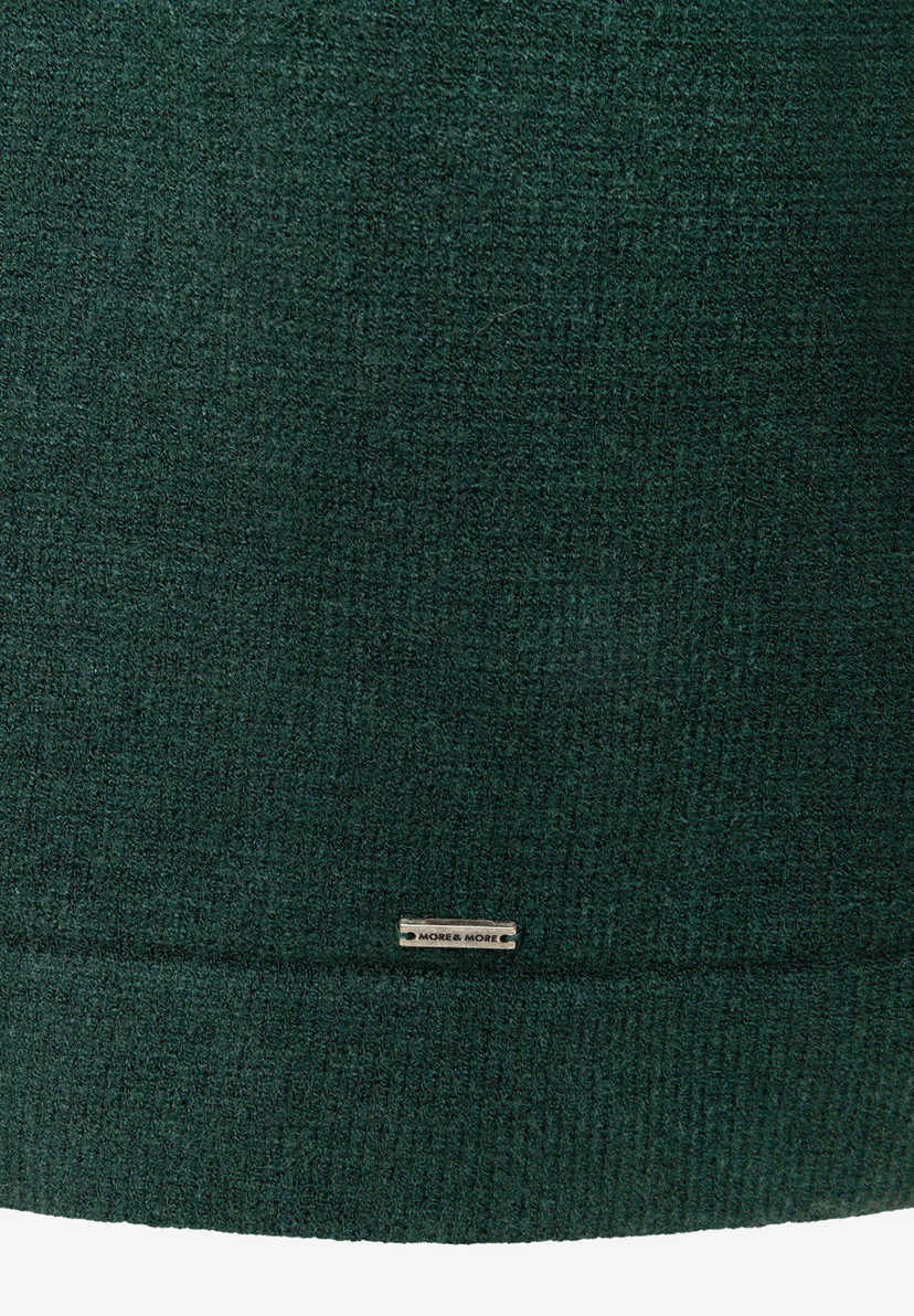 Dunkelgrünes Strickkleid von MORE & MORE mit geripptem Saum und Markenplakette, Nahaufnahme der Stoffstruktur.