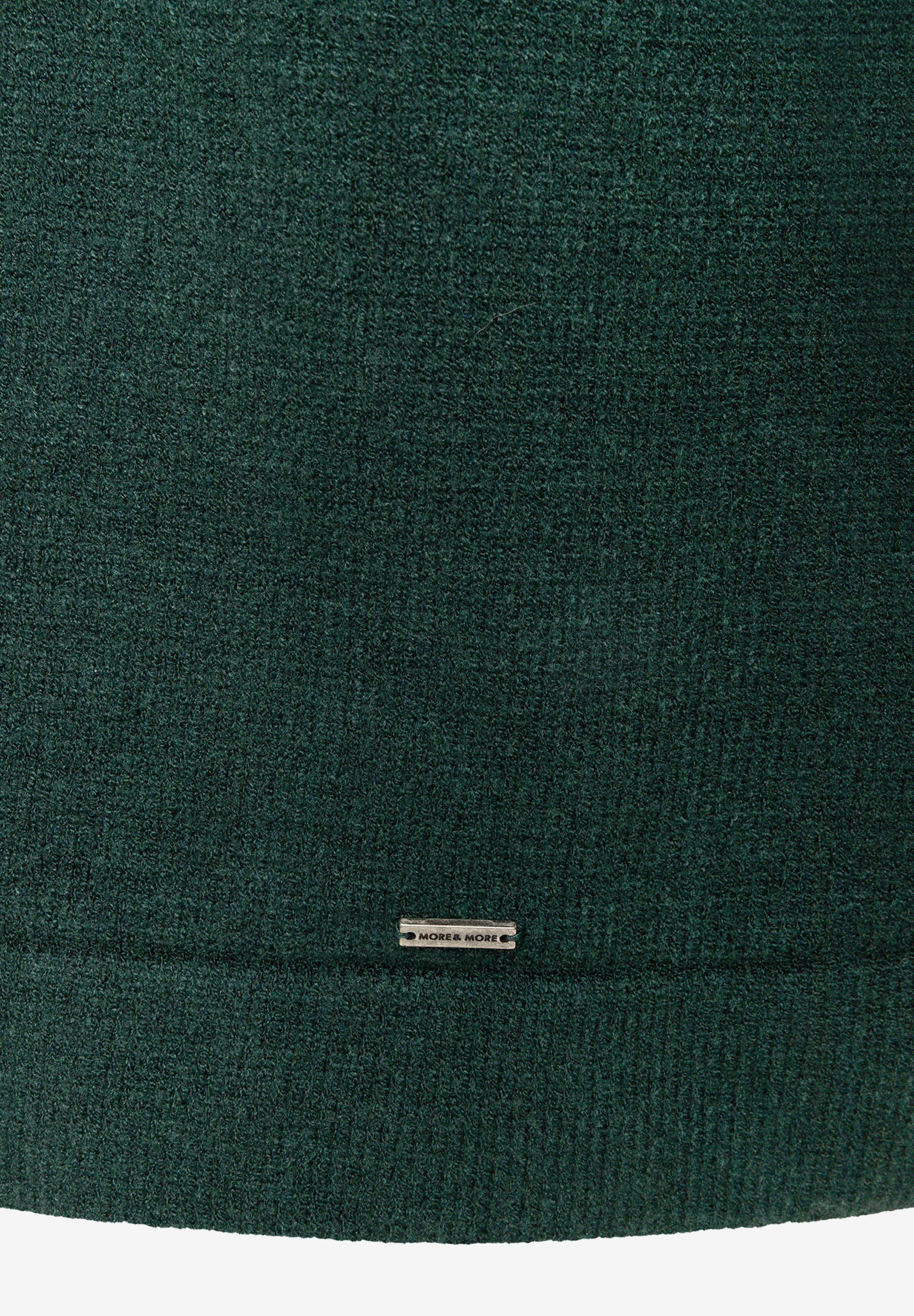Dunkelgrünes Strickkleid von MORE & MORE mit geripptem Saum und Markenplakette, Nahaufnahme der Stoffstruktur. Dunkelgrünes Strickkleid von MORE & MORE mit geripptem Saum und Markenplakette, Nahaufnahme der Stoffstruktur.