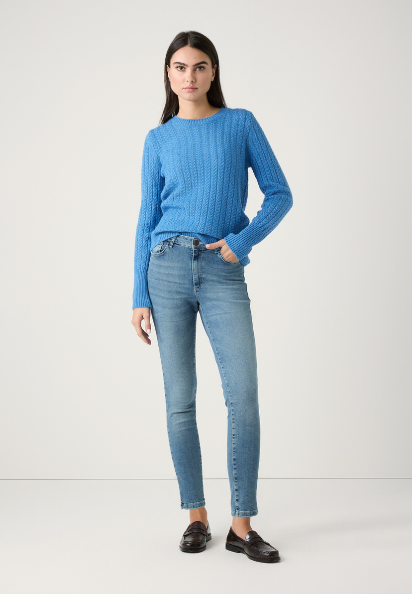 Eine Frau in MORE & MORE Oberteilen: blauem Strickpullover und Jeans, posiert vor einem hellen Hintergrund. Eine Frau in MORE & MORE Oberteilen: blauem Strickpullover und Jeans, posiert vor einem hellen Hintergrund.