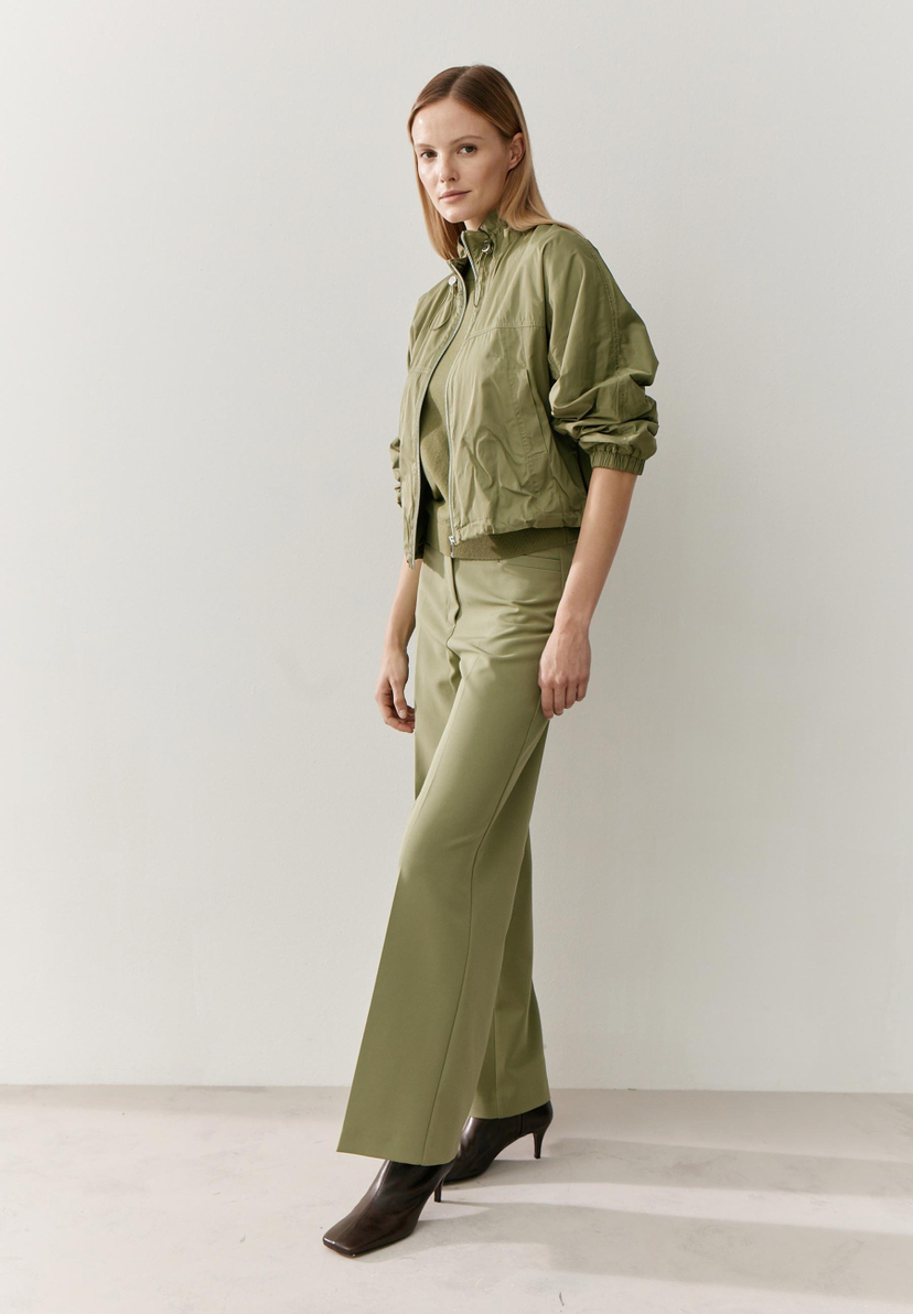 Eine Frau in einem grünen MORE & MORE Oberteil (Blazer) aus Webware mit glänzender Optik. Eine Frau in einem grünen MORE & MORE Oberteil (Blazer) aus Webware mit glänzender Optik.