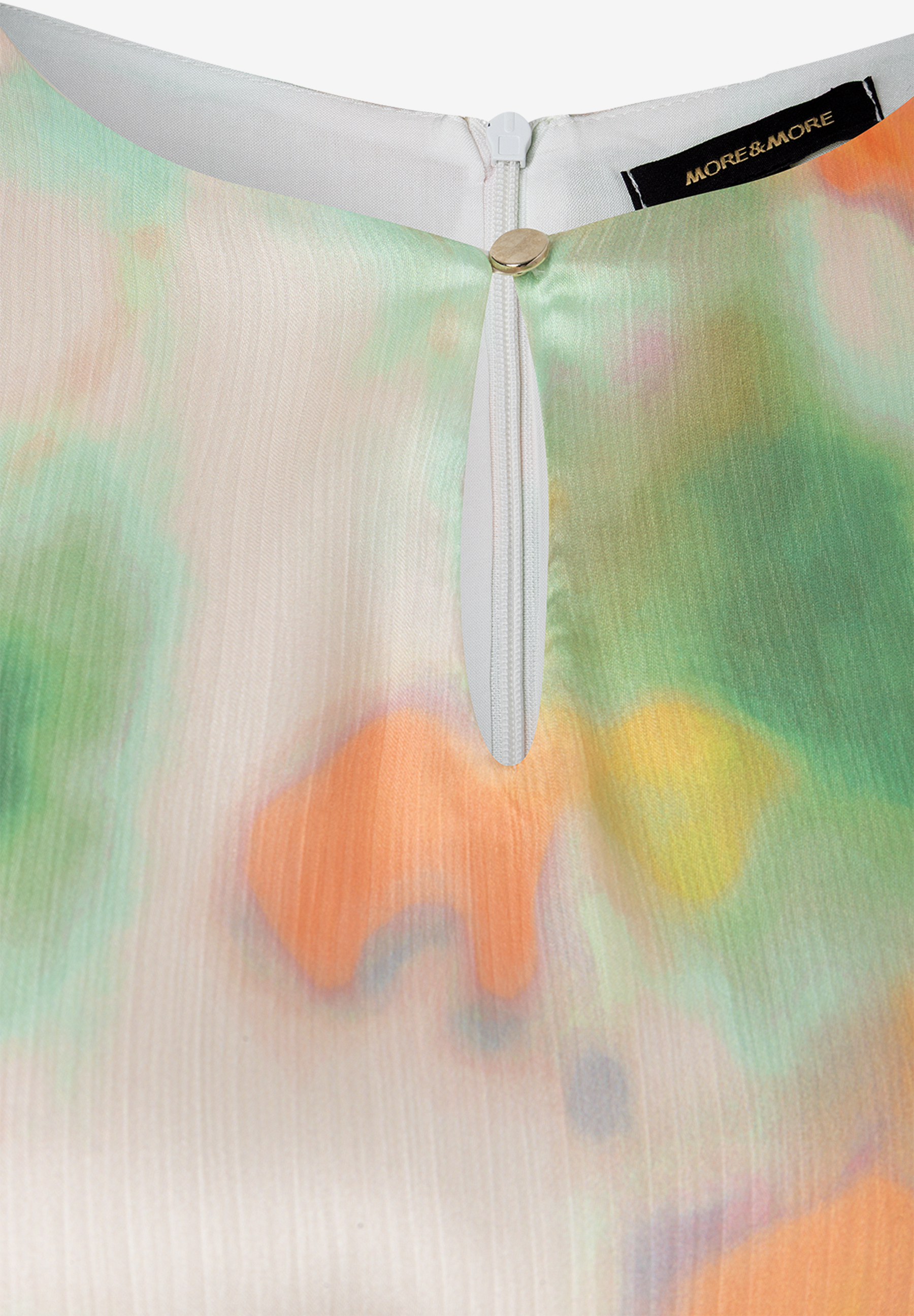 Detailansicht eines MORE & MORE Oberteils aus Chiffon mit Reißverschluss und Etikett. Detailansicht eines MORE & MORE Oberteils aus Chiffon mit Reißverschluss und Etikett.