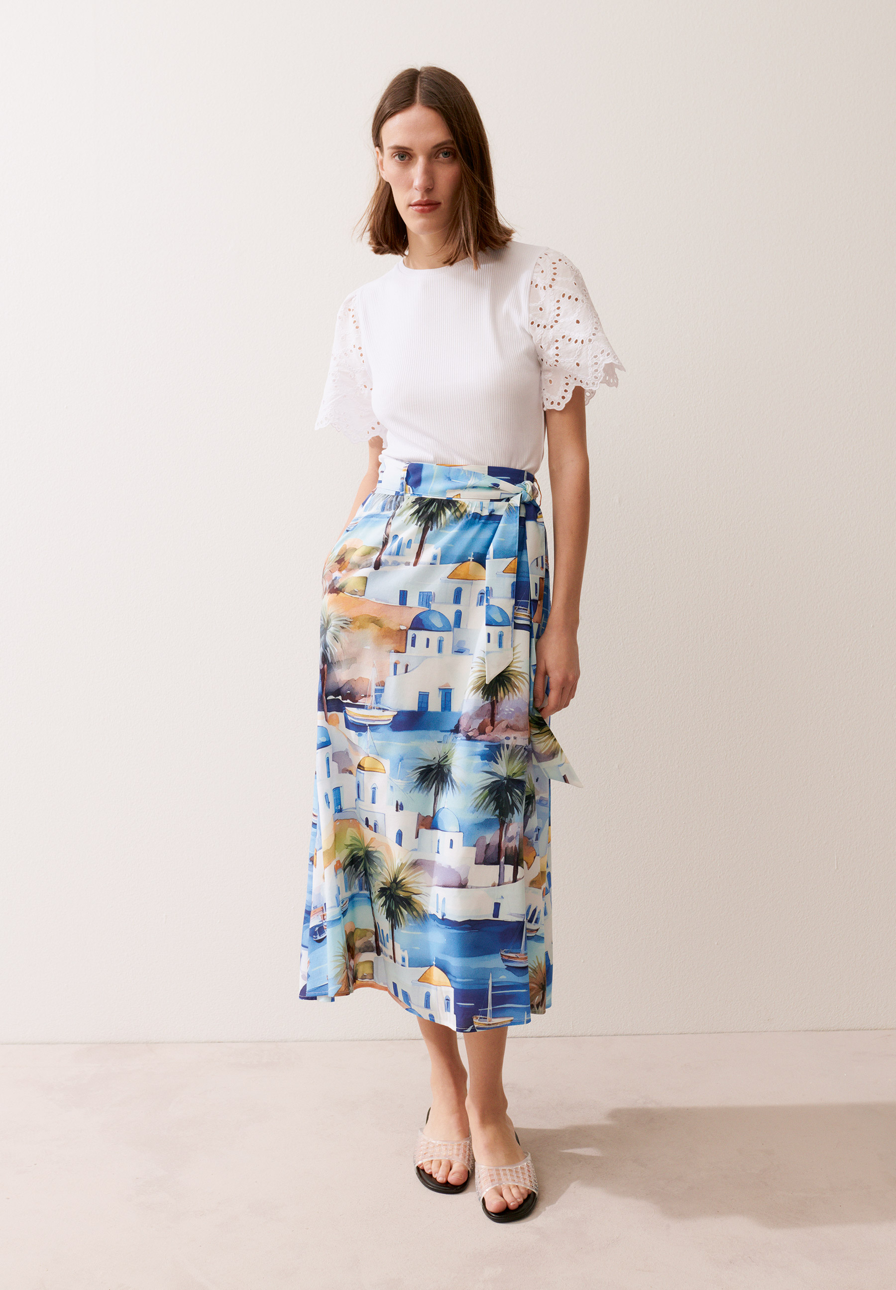 Eine Frau mit einem MORE & MORE-Top und einem blau-weißen Rock mit Strandmotiven posiert. Eine Frau mit einem MORE & MORE-Top und einem blau-weißen Rock mit Strandmotiven posiert.