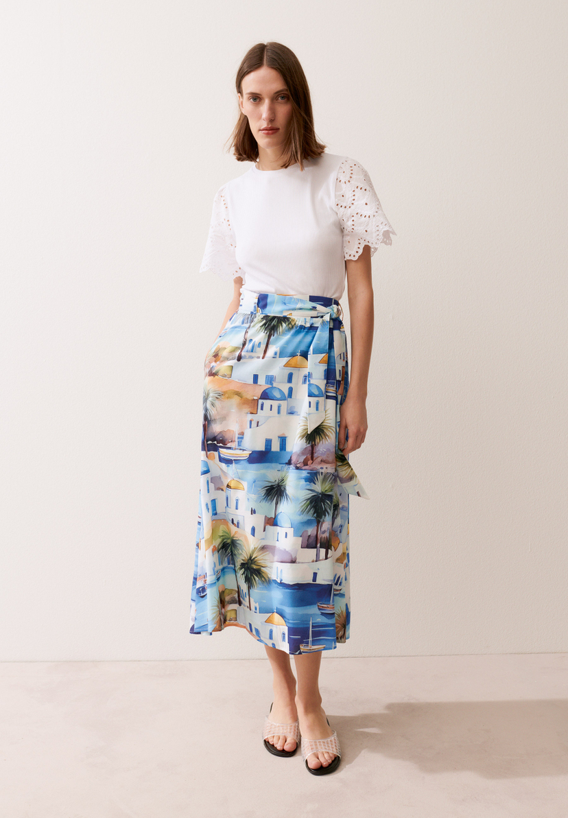 Eine Frau mit einem MORE & MORE-Top und einem blau-weißen Rock mit Strandmotiven posiert. Eine Frau mit einem MORE & MORE-Top und einem blau-weißen Rock mit Strandmotiven posiert.