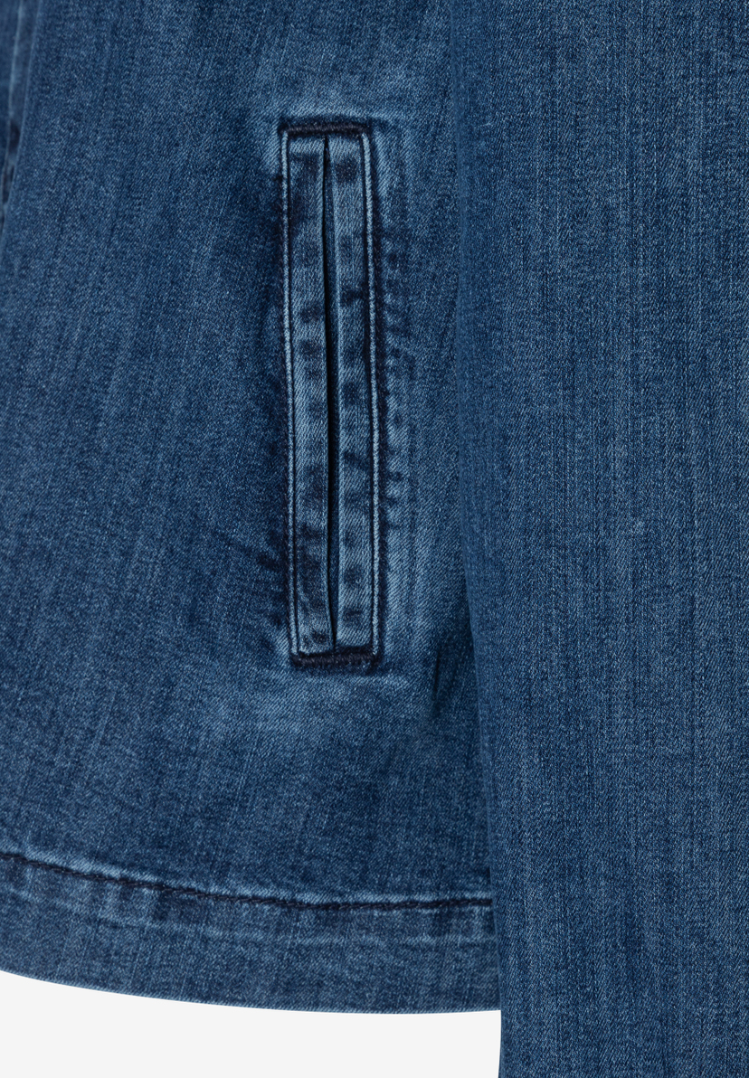 Nahaufnahme eines blauen MORE & MORE Blasers aus Denimstoff mit einer kleinen Tasche. Nahaufnahme eines blauen MORE & MORE Blasers aus Denimstoff mit einer kleinen Tasche.