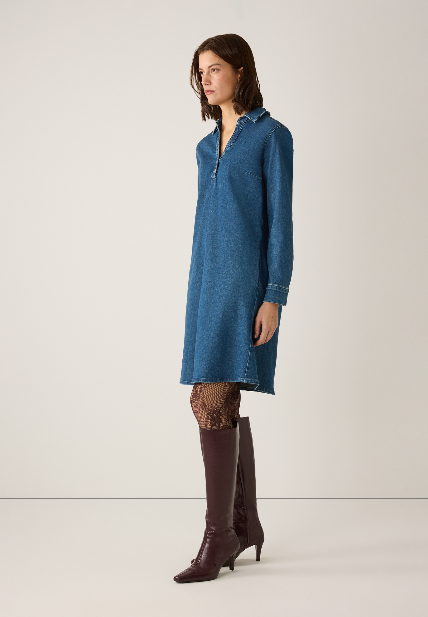 Eine Frau im MORE & MORE-Denimkleid mit braunen Stiefeln und gemusterter Strumpfhose. Eine Frau im MORE & MORE-Denimkleid mit braunen Stiefeln und gemusterter Strumpfhose.