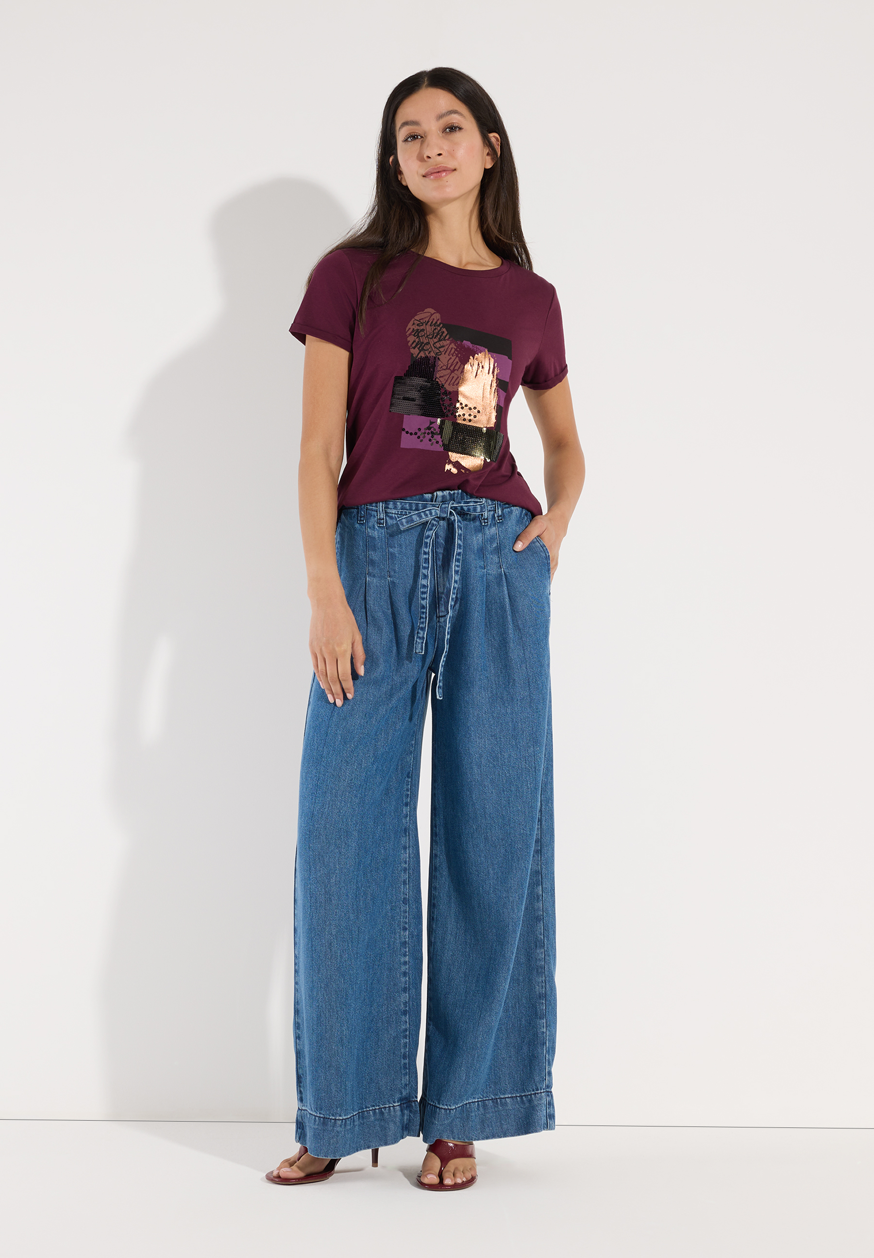 MORE & MORE T-Shirt mit Print in Dunkelrot, kombiniert mit ausgestellten Jeans und hochhackigen Sandalen. MORE & MORE T-Shirt mit Print in Dunkelrot, kombiniert mit ausgestellten Jeans und hochhackigen Sandalen.