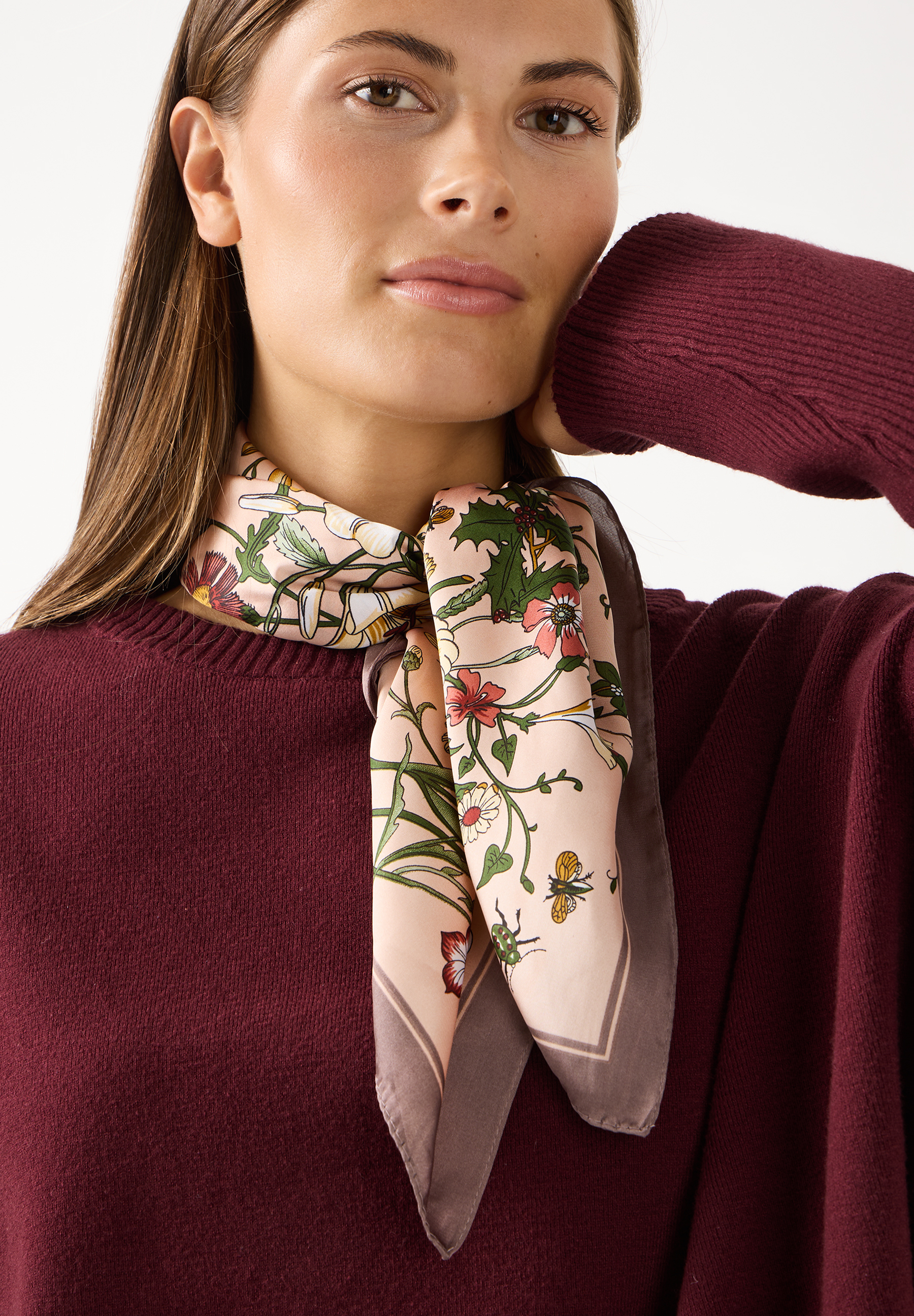 MORE & MORE Accessoires: Blonder Frau trägt ein beigefarbenes Tuch mit Blumenmuster und einen bordeauxroten Pullover.