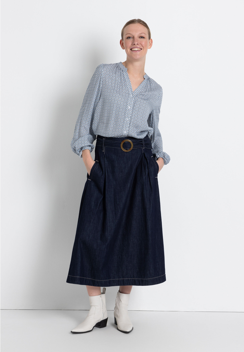 Eine Frau in einer MORE & MORE Bluse mit Muster und einem dunklen Rock. Sie trägt weiße Stiefeletten. Eine Frau in einer MORE & MORE Bluse mit Muster und einem dunklen Rock. Sie trägt weiße Stiefeletten.