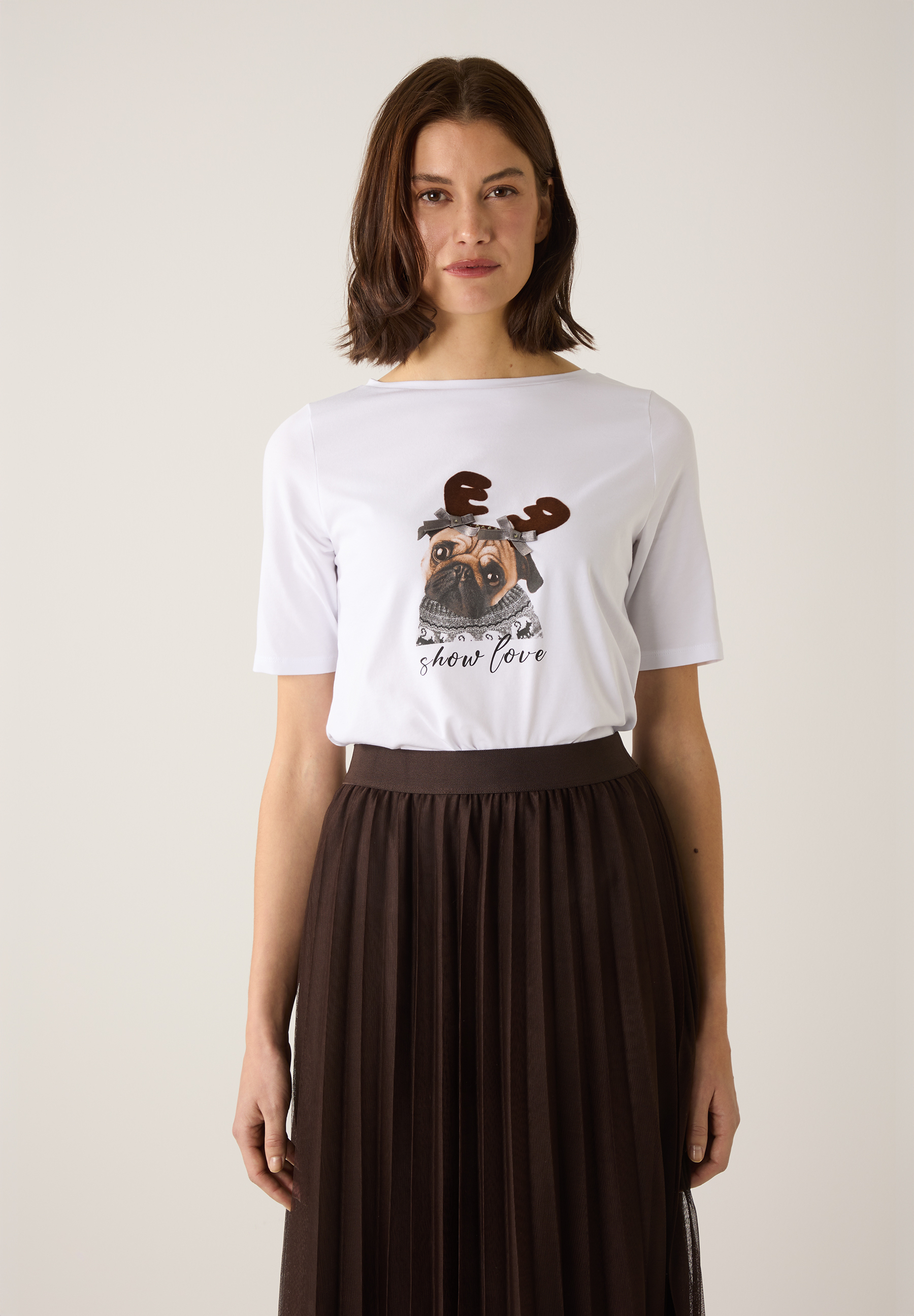 Eine Frau mit MORE & MORE Oberteil mit Mops-Motiv und braunem Faltenrock.