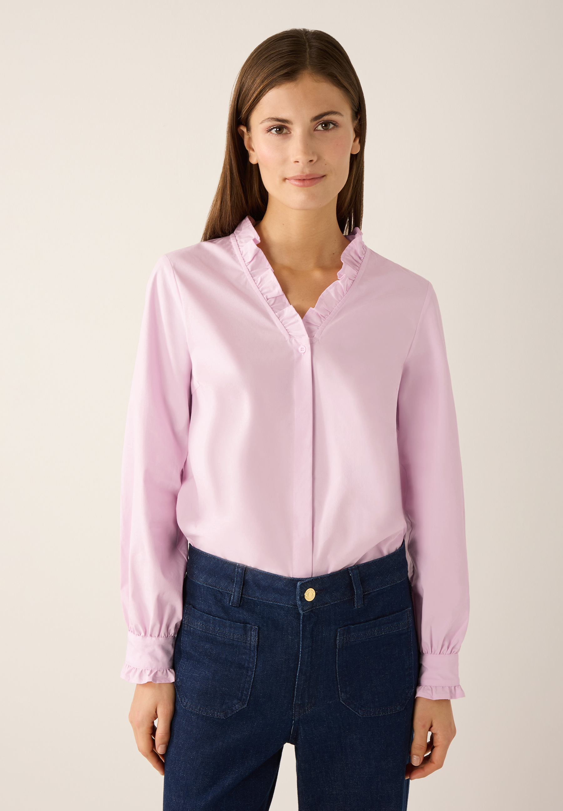 Eine Frau trägt eine rosa MORE & MORE Bluse mit Rüschen und Jeans.