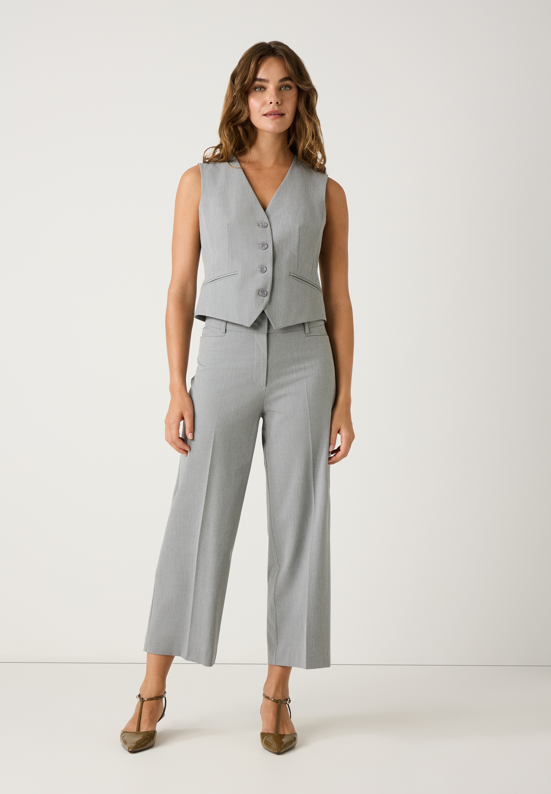 Eine Frau trägt ein graues Hosenanzug-Set von MORE & MORE. Der Blazer ist ärmellos und mit Knöpfen versehen. Das Set besteht aus Viskosemischgewebe. Eine Frau trägt ein graues Hosenanzug-Set von MORE & MORE. Der Blazer ist ärmellos und mit Knöpfen versehen. Das Set besteht aus Viskosemischgewebe.