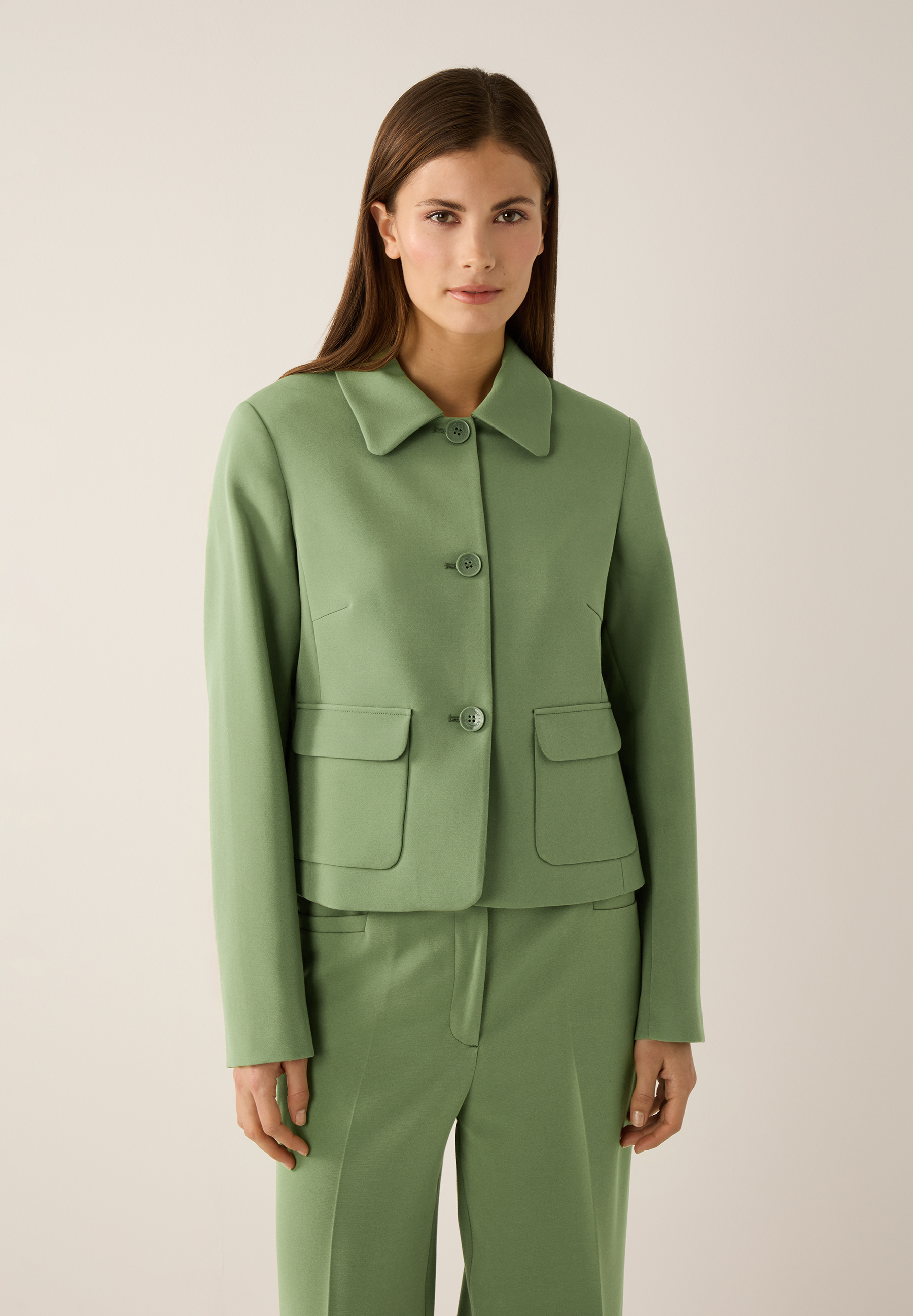 Eine Frau trägt einen grünen Blazer von MORE & MORE mit passender Hose. Der Blazer ist aus Webware und hat einen angenehmen Tragekomfort.