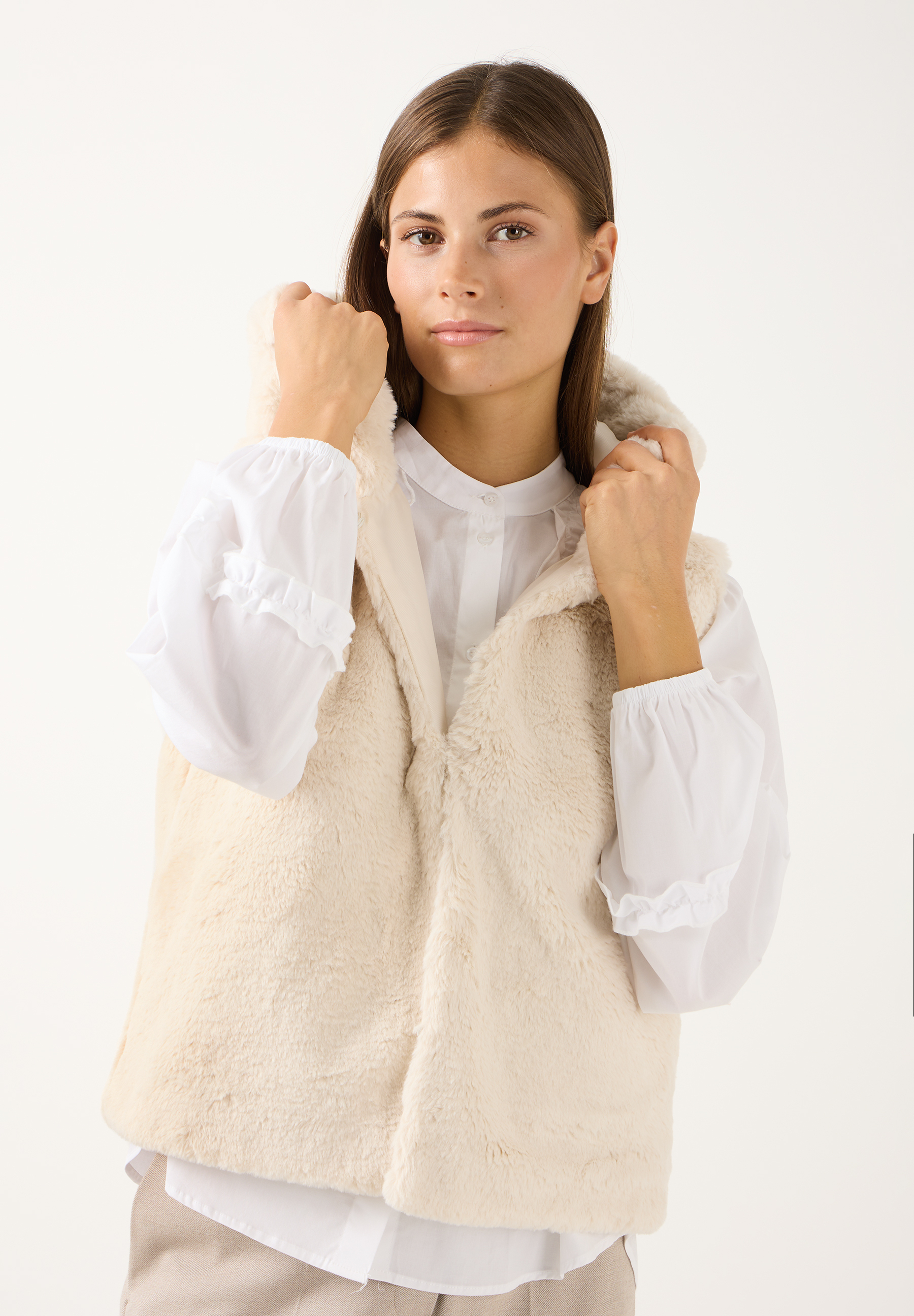 MORE & MORE Damen-Weste: Eine junge Frau trägt eine cremefarbene Teddyfell-Weste mit Kapuze über einer weißen Bluse.