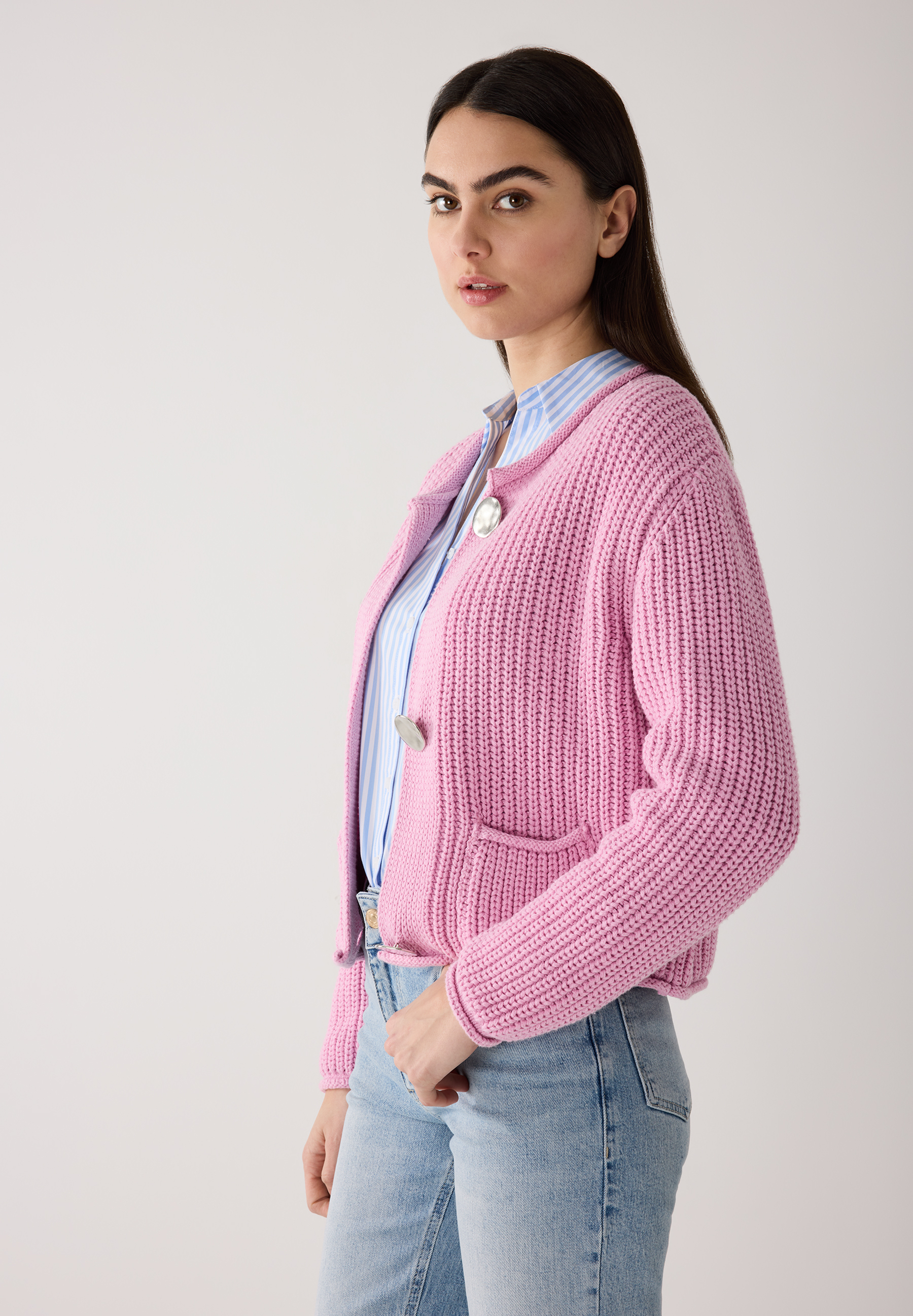 Eine Frau trägt einen pinken MORE & MORE Cardigan aus Rippstrick über einem blau-weiß gestreiften Oberteil und Jeans.
