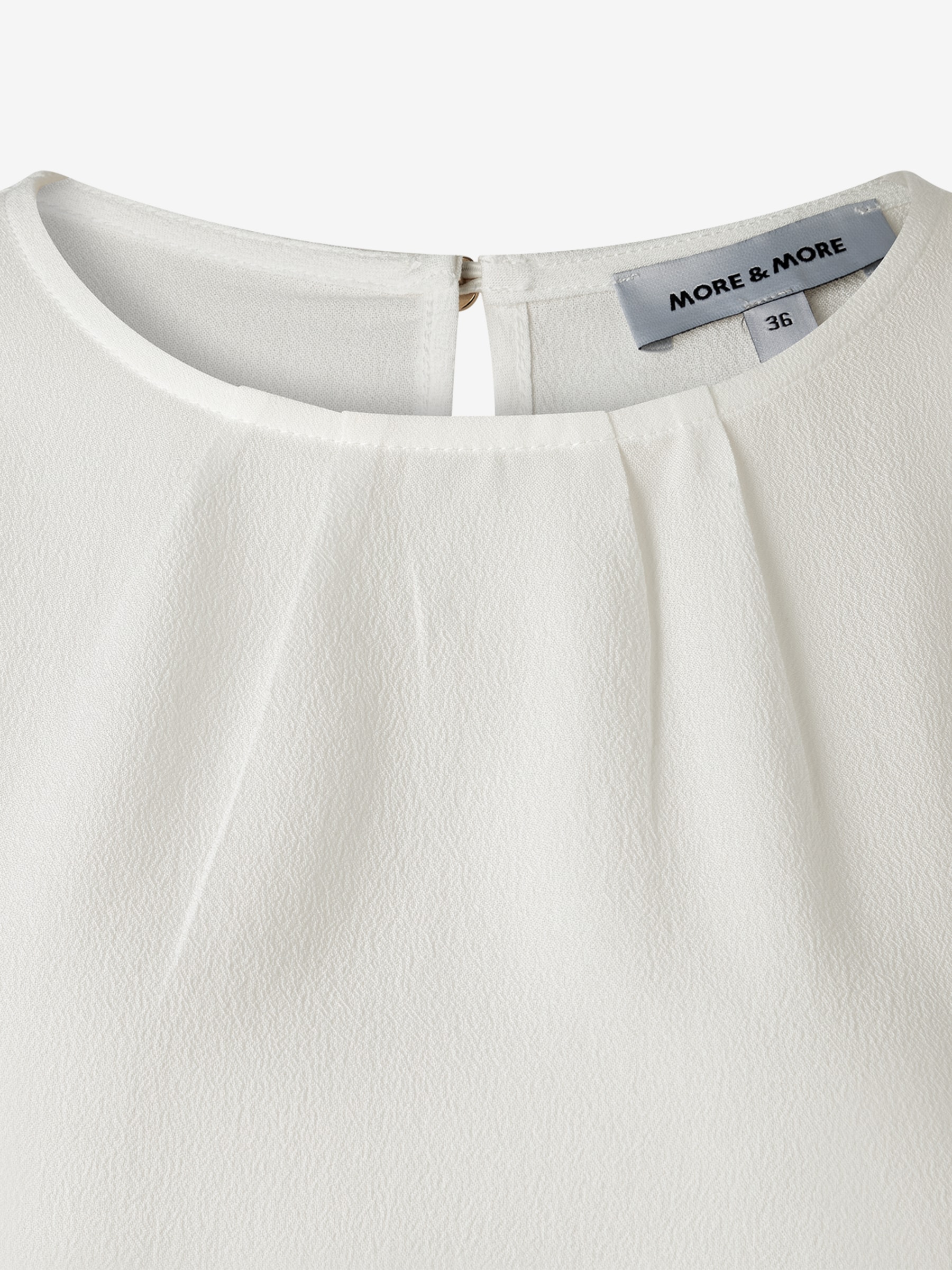 Detailaufnahme einer weißen MORE & MORE Bluse mit Kragen und Etikett in Größe 36. Detailaufnahme einer weißen MORE & MORE Bluse mit Kragen und Etikett in Größe 36.