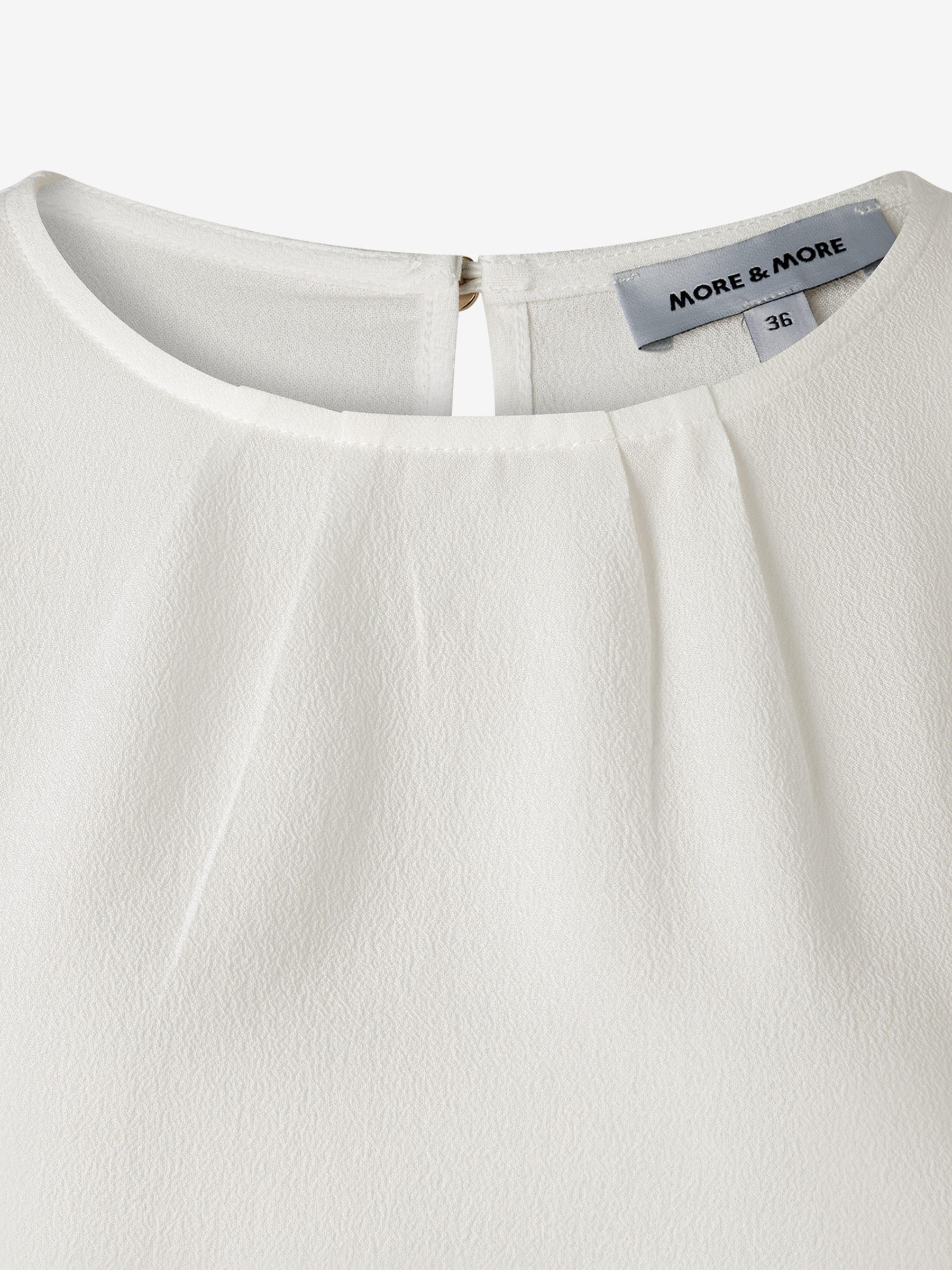 Nahaufnahme einer weißen MORE & MORE Bluse aus Viskose-Crêpe mit rundem Ausschnitt und angedeuteten Kellerfalten. Nahaufnahme einer weißen MORE & MORE Bluse aus Viskose-Crêpe mit rundem Ausschnitt und angedeuteten Kellerfalten.
