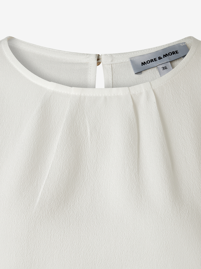 Nahaufnahme einer weißen MORE & MORE Bluse aus Viskose-Crêpe mit rundem Ausschnitt und angedeuteten Kellerfalten. Nahaufnahme einer weißen MORE & MORE Bluse aus Viskose-Crêpe mit rundem Ausschnitt und angedeuteten Kellerfalten.