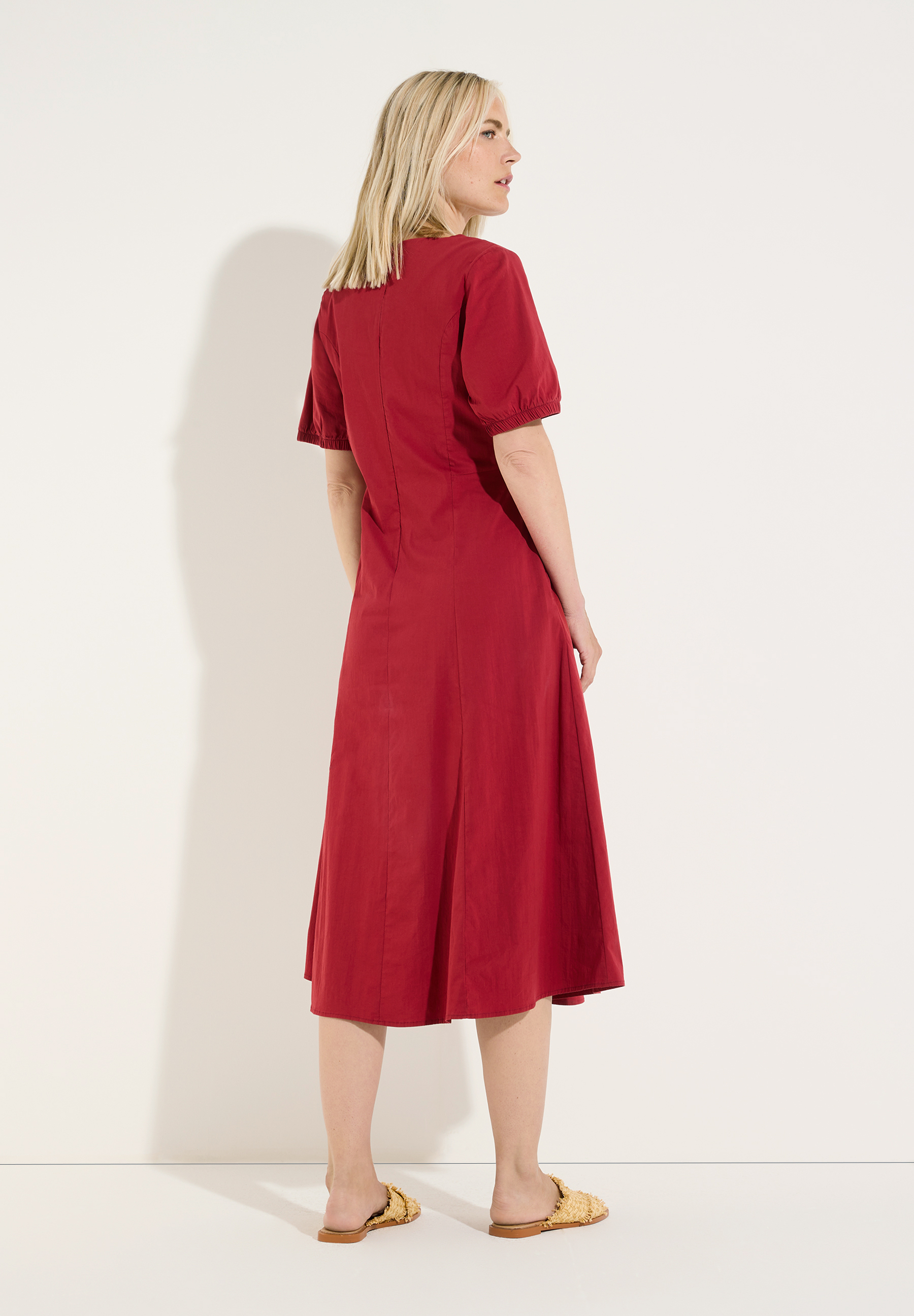 MORE & MORE rotes Kleid, ein blondes Model präsentiert das Kleid auf einem weißen Hintergrund, Seitenansicht. MORE & MORE rotes Kleid, ein blondes Model präsentiert das Kleid auf einem weißen Hintergrund, Seitenansicht.